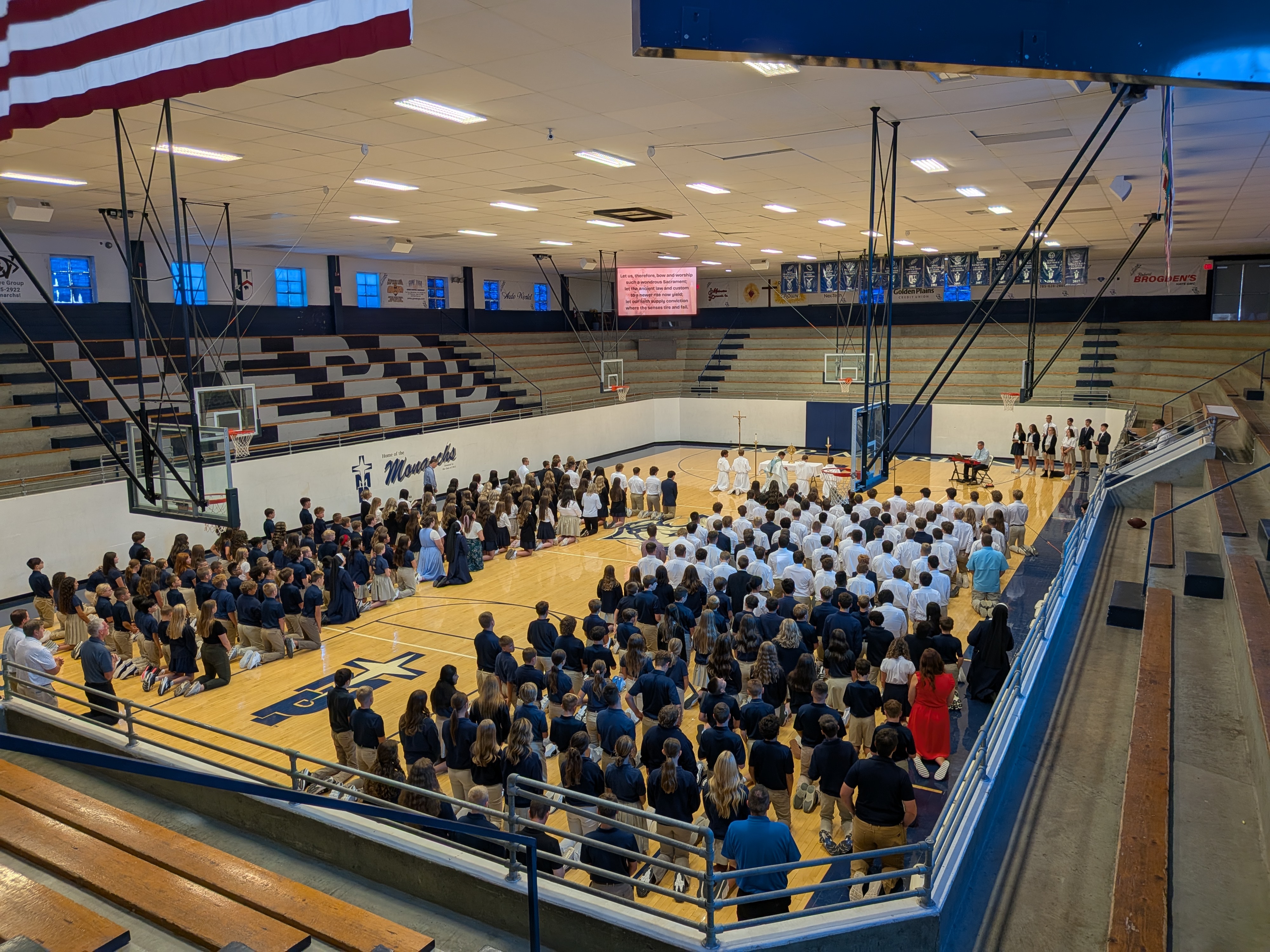 Adoration in gymnasium with many students kneeling on the floor