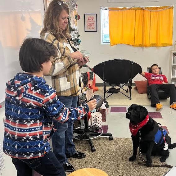 Adults and students work with a black Labrador Retriever 