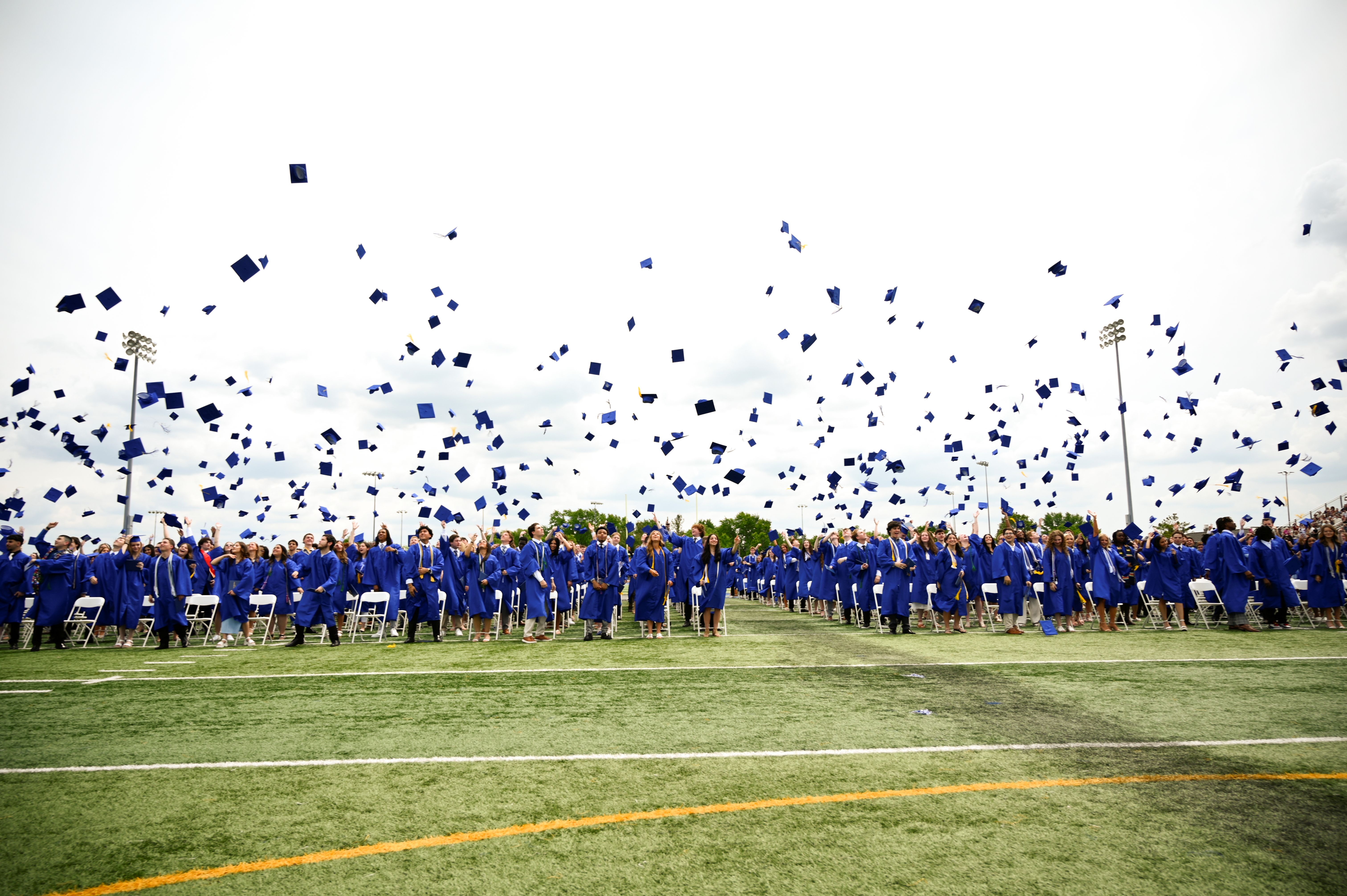 Many people in blue caps throw them into the air on a field with yellow markings.