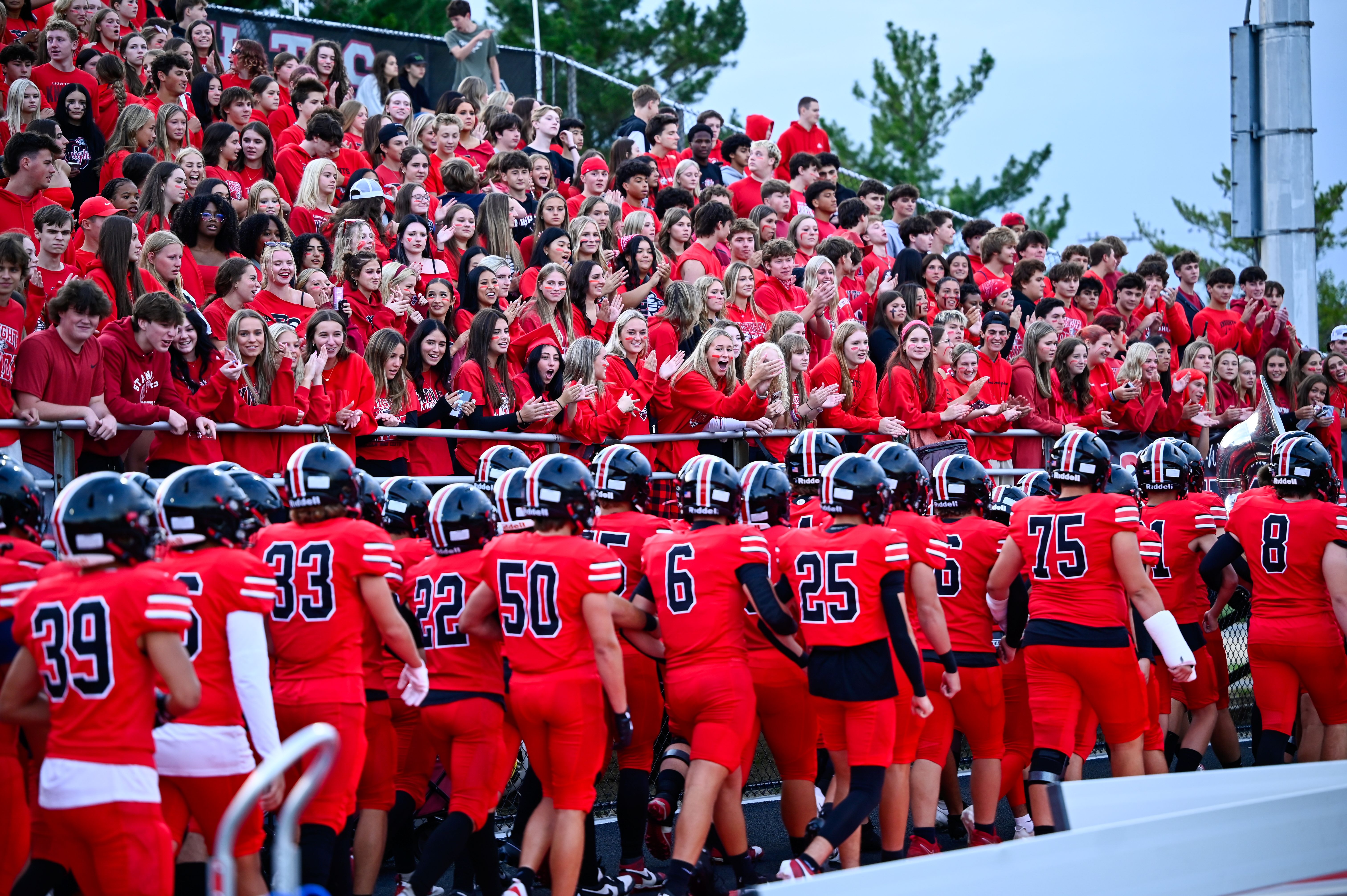 A wide angle view of football players on the field and students in the bleachers all wearing red