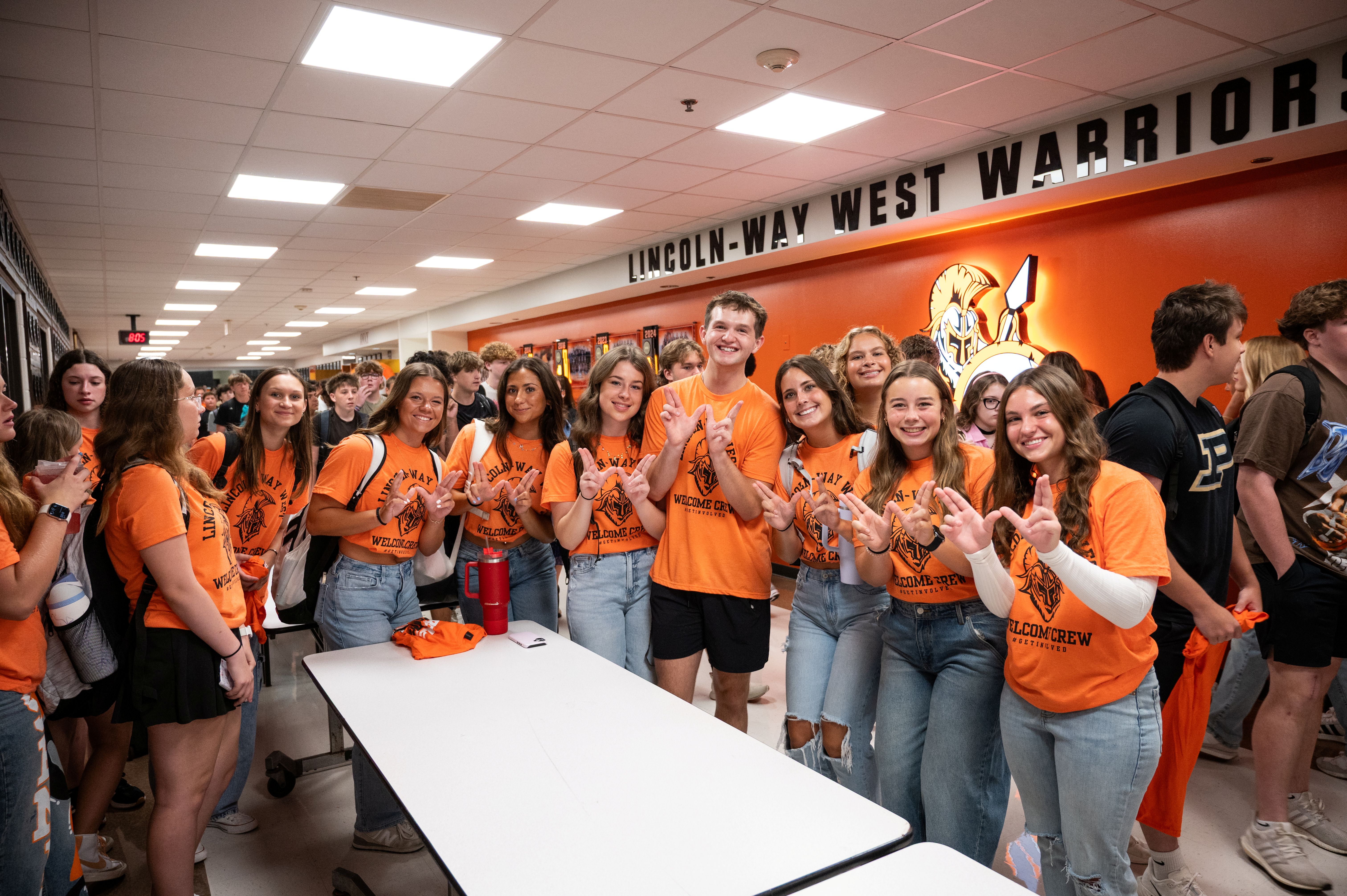 Students in all orange standing around a table smiling