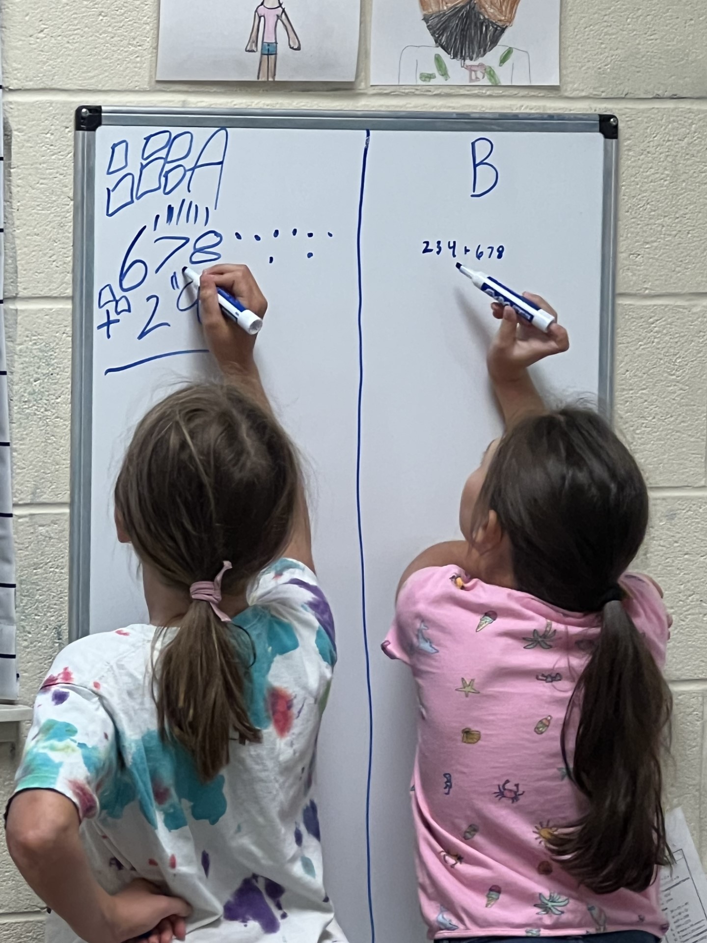 the back of two girls as they write on the 360 math boards