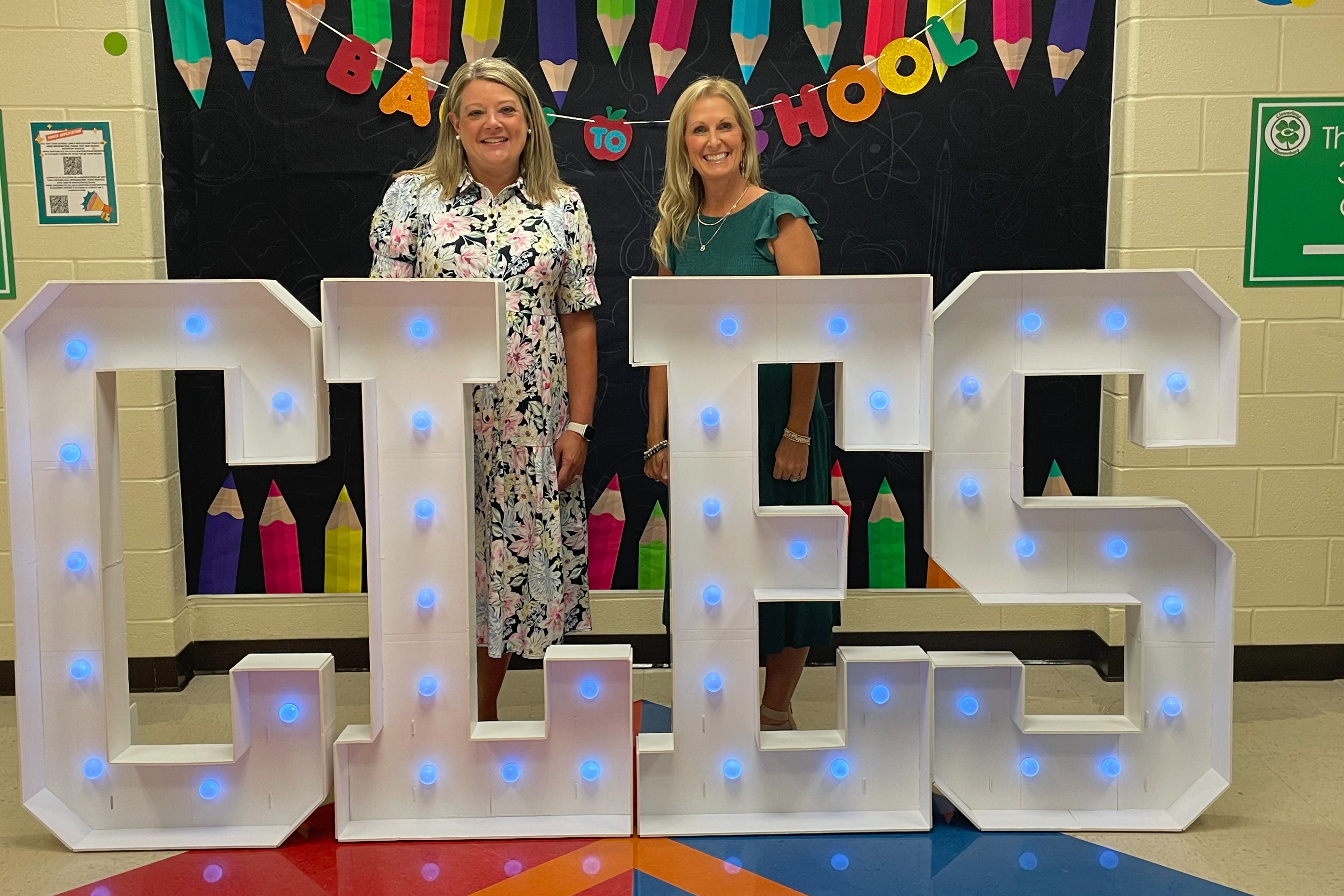 Mrs. O'Tinger and Mrs. Gravitt are facing the camera and smiling while standing in front of a Back to School set up.