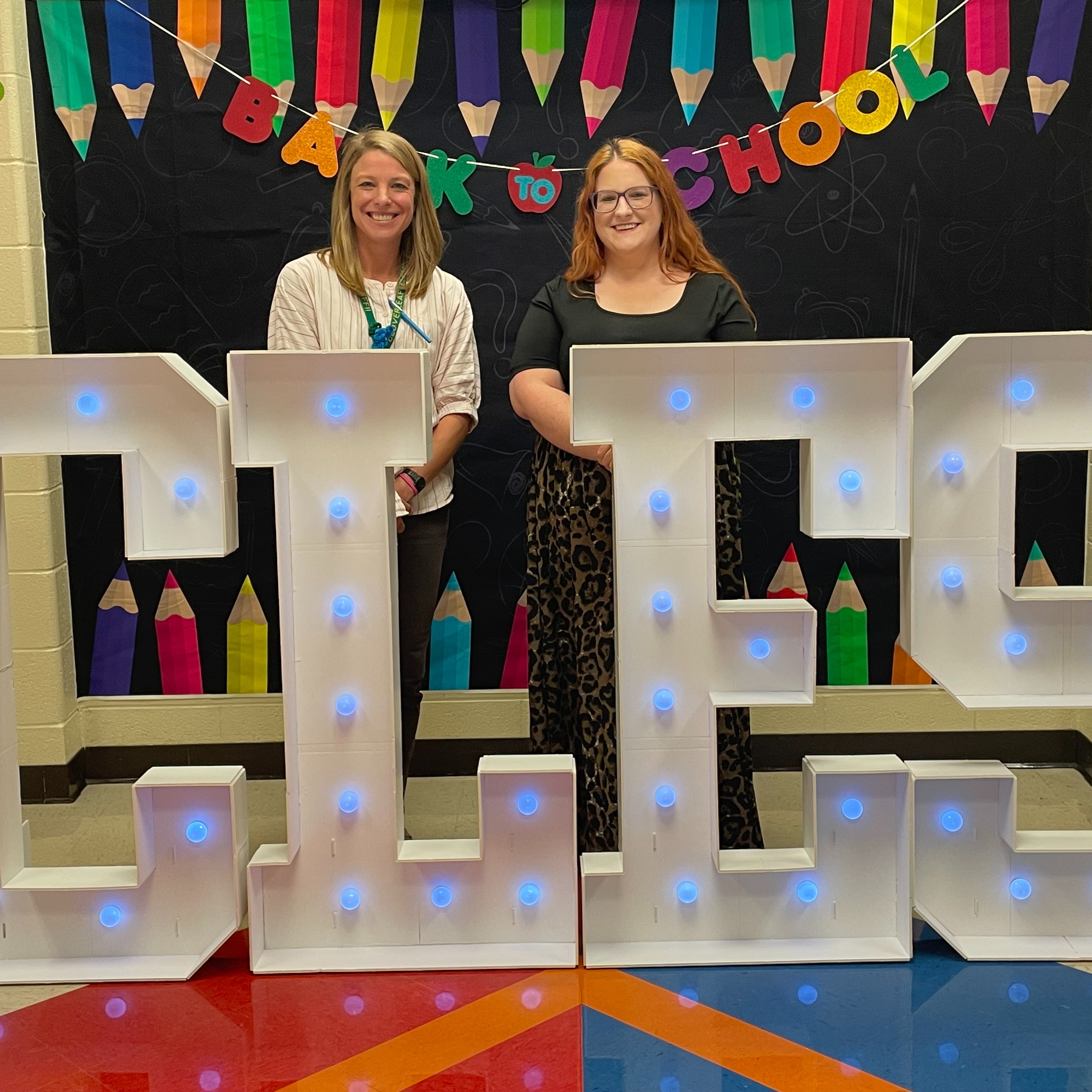 Mrs. Tripp and Mrs. Bollinger smiling at the camera in front of the Back to School display