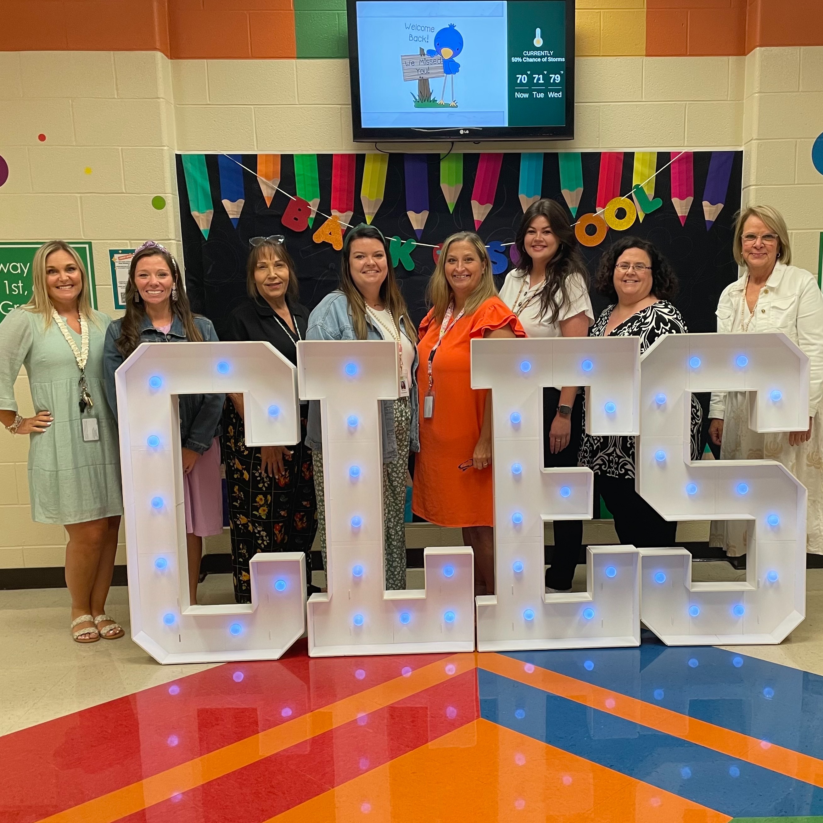 Eight smiling female educators facing the camera in front of a Back to School display