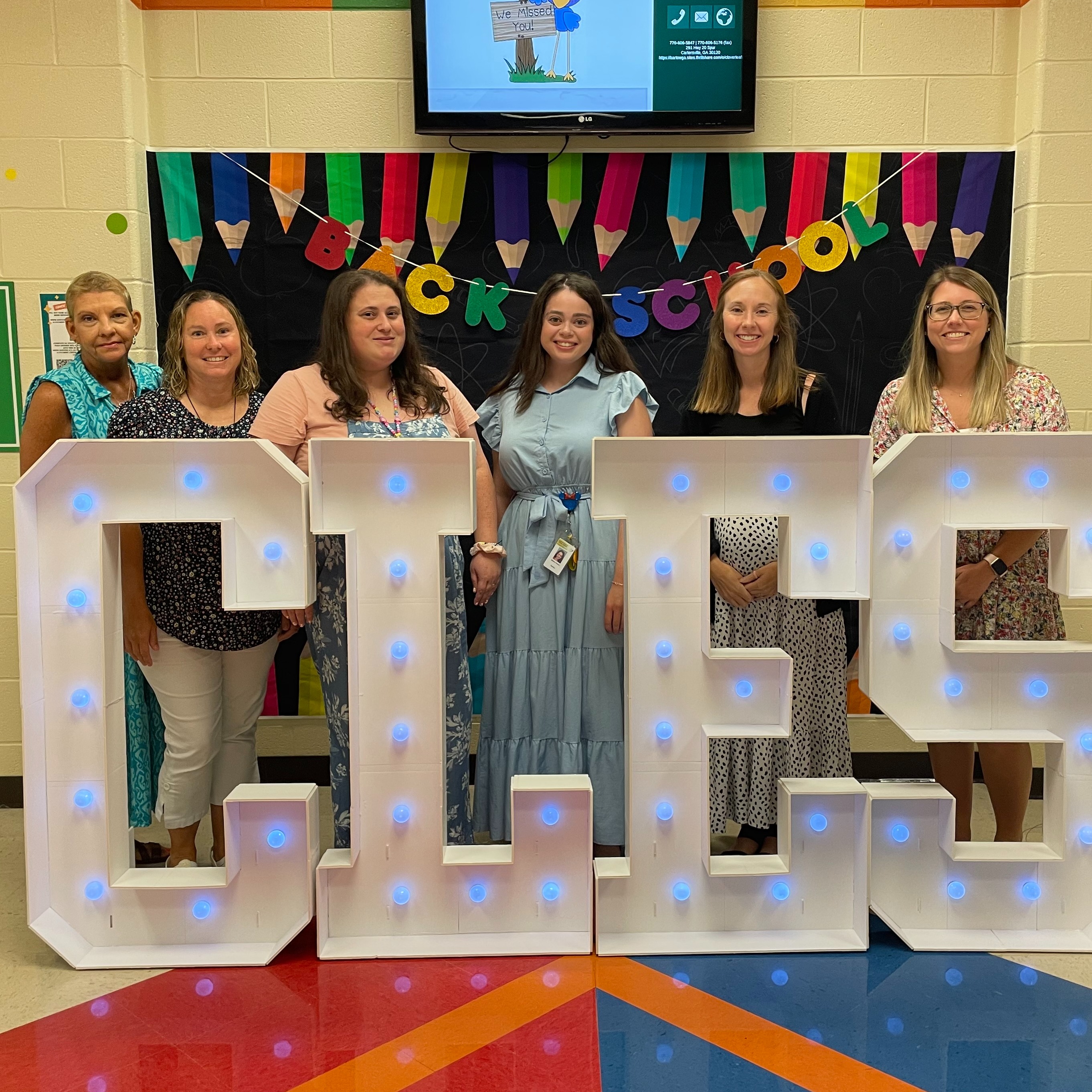Six smiling female educators posing for the camera in front of a Back to School set up