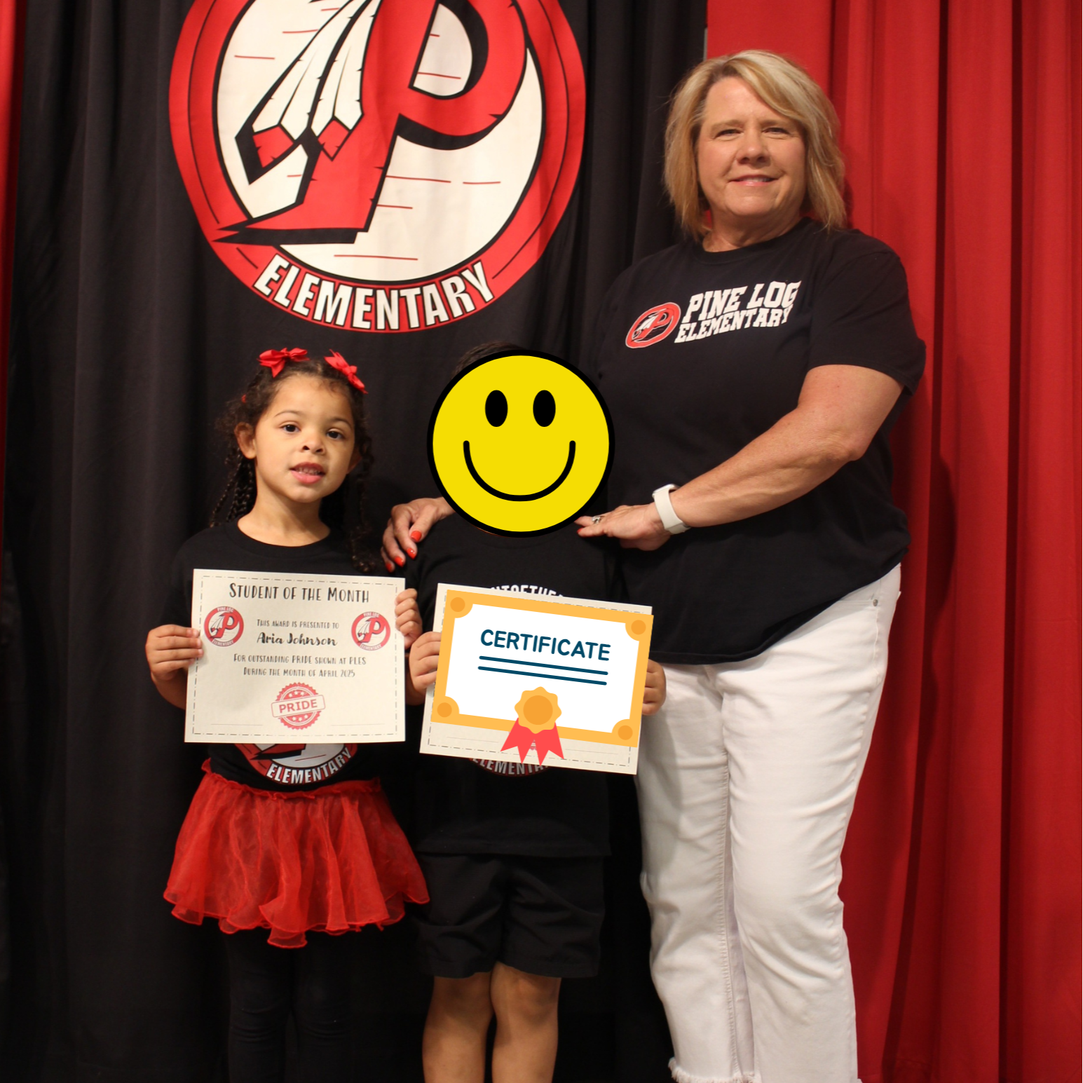 One adult and 2 children  standing on stage holding awards for student of the month.