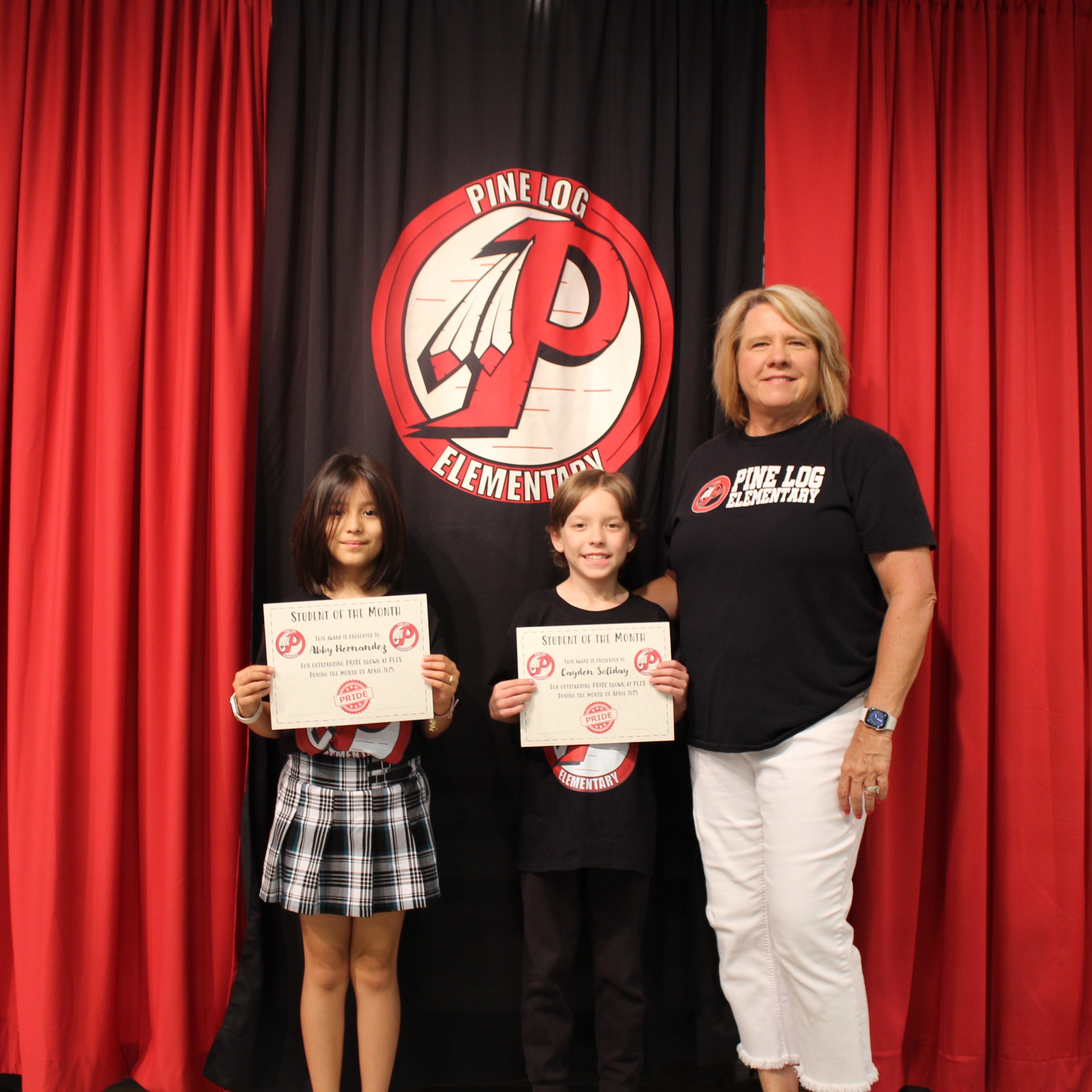 One adult and 2 children  standing on stage holding awards for student of the month.