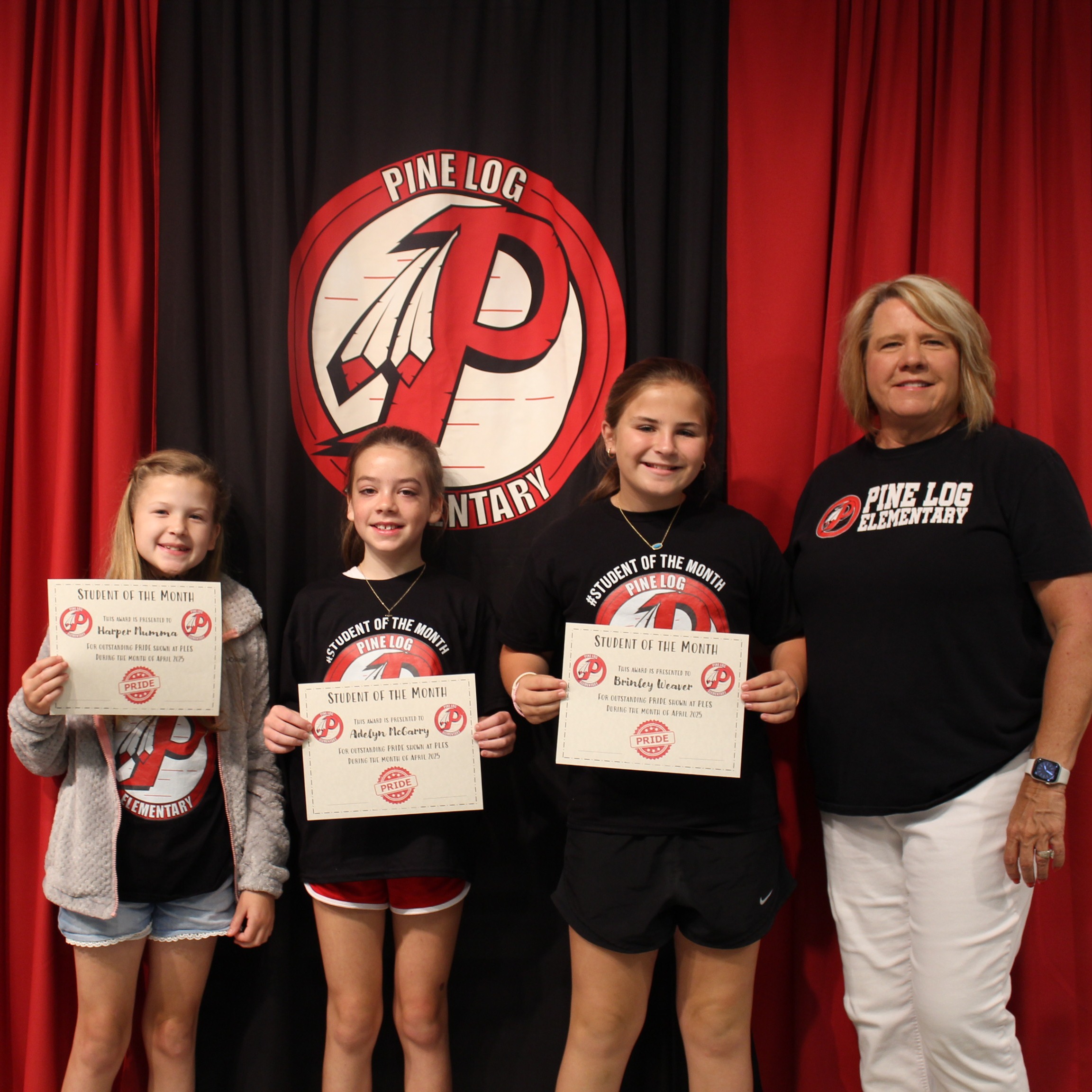 One adult and 3 children  standing on stage holding awards for student of the month.