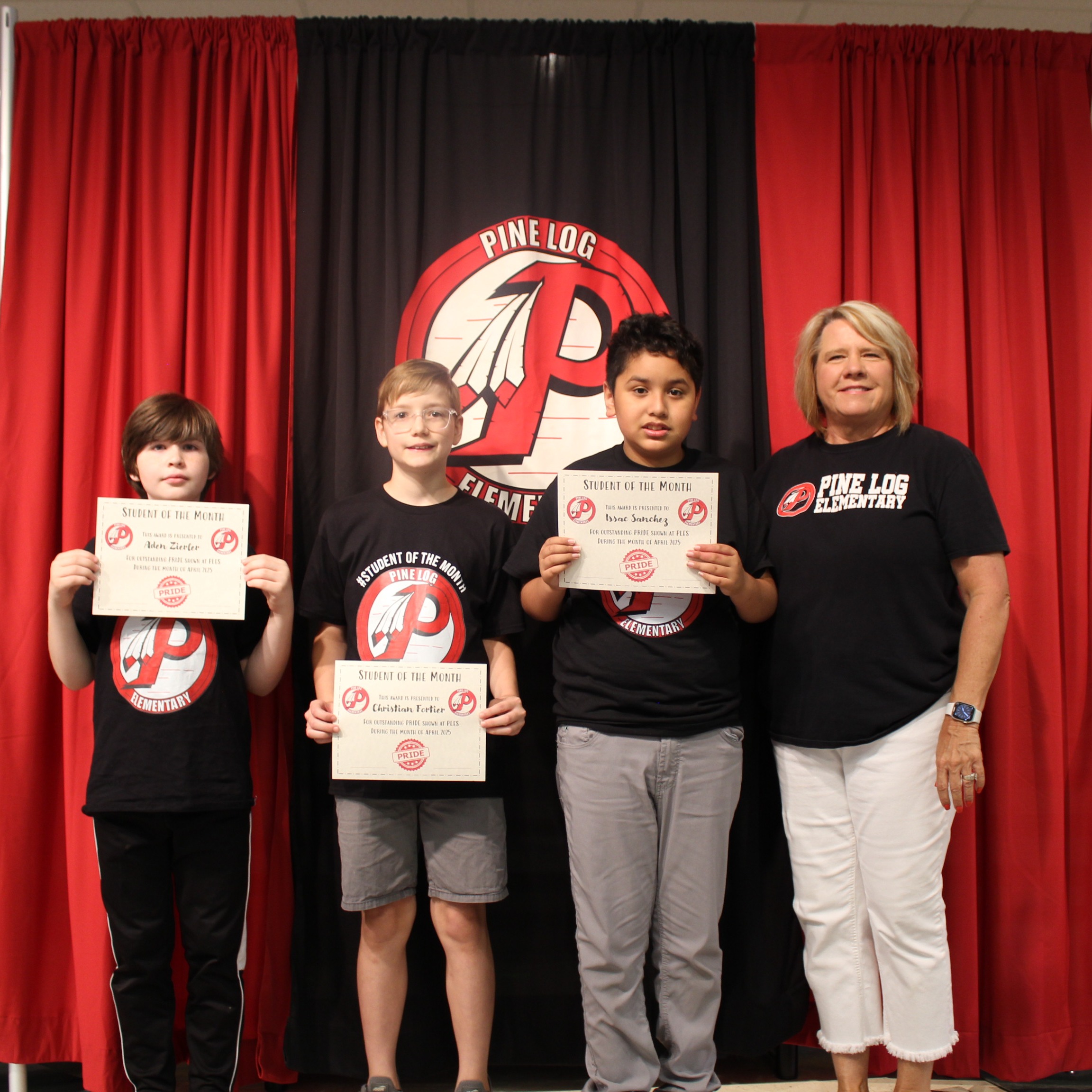 One adult and 3 children  standing on stage holding awards for student of the month.