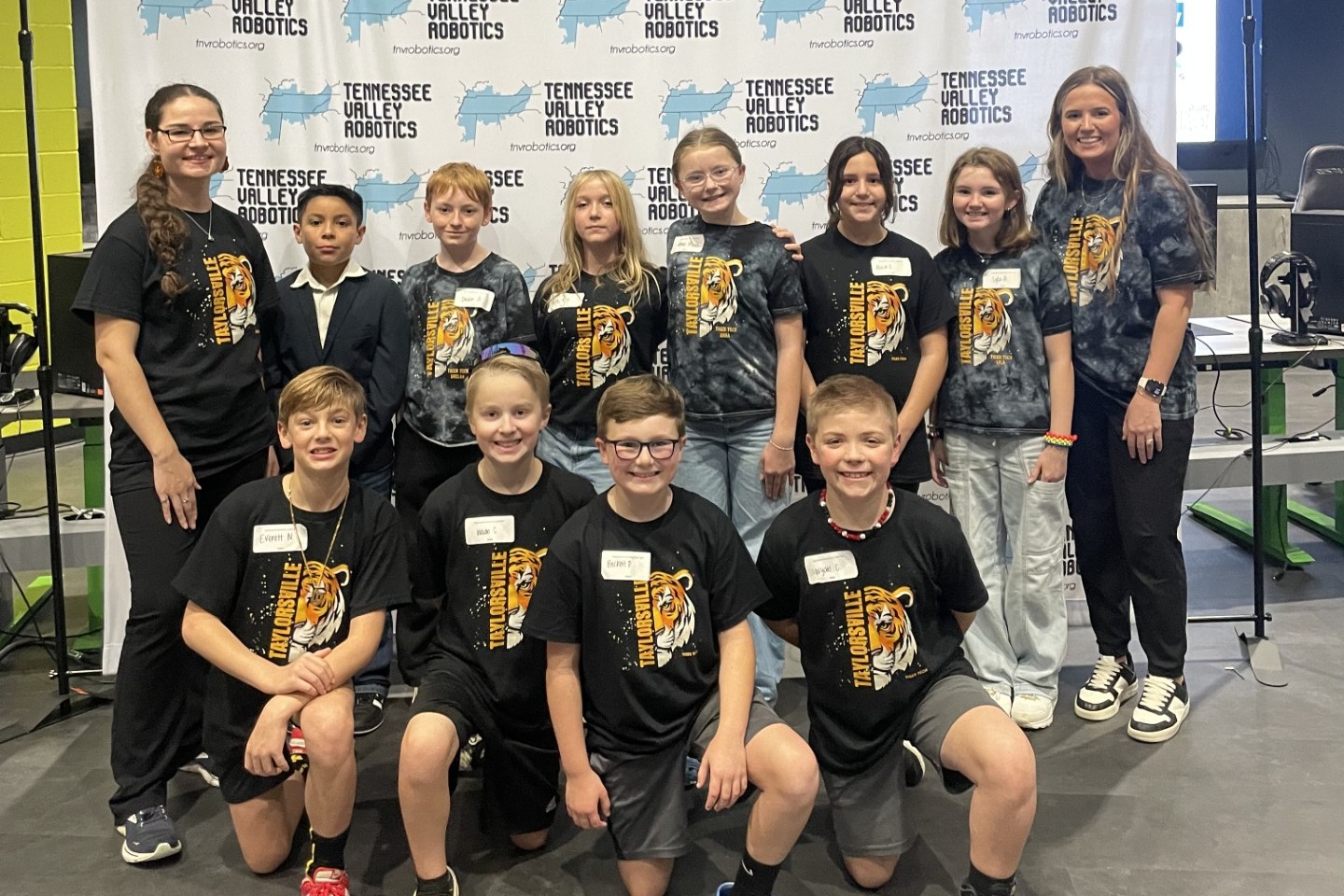 A group of students in matching shirts poses for a photo in front of a promotional banner.