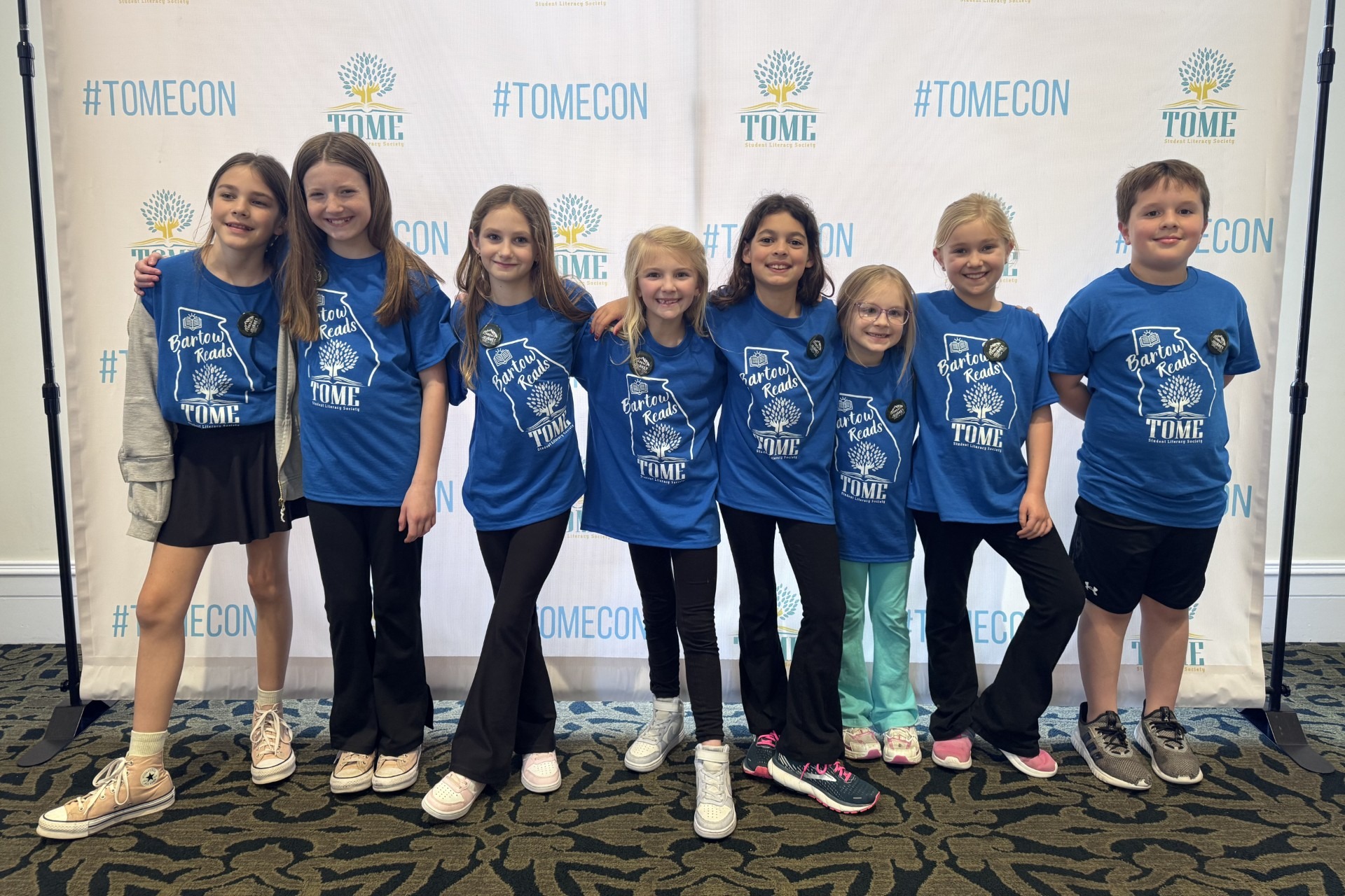 Group of young people in matching blue t-shirts posing in front of a white backdrop.