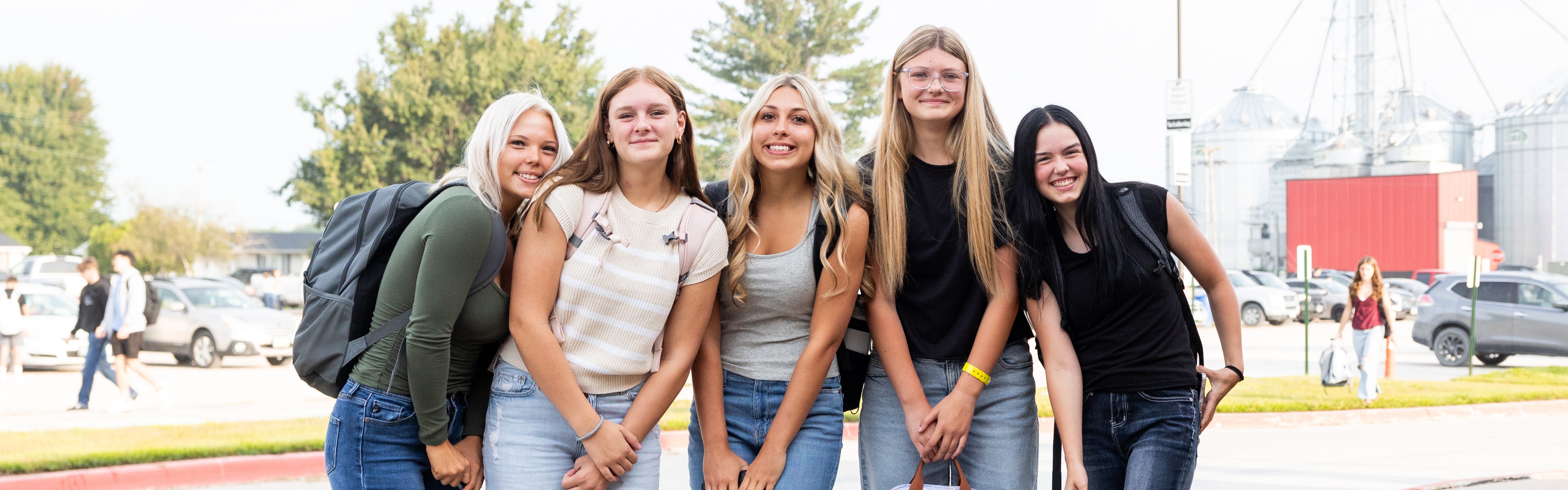 Five female students pose together outside on of school on a sunny day