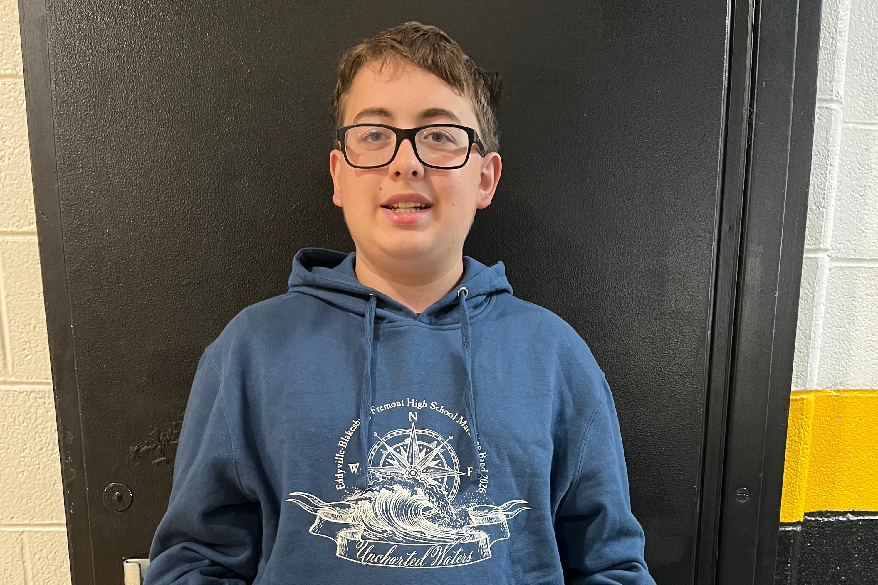 Jr./Sr. High Student of the Week posed for a portrait against a school hallway wall with black and gold accent stripes.