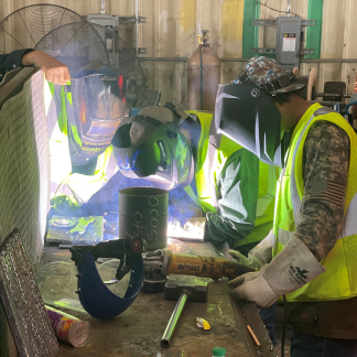 Image of kids in a shop wearing neon vest and welding helmets 