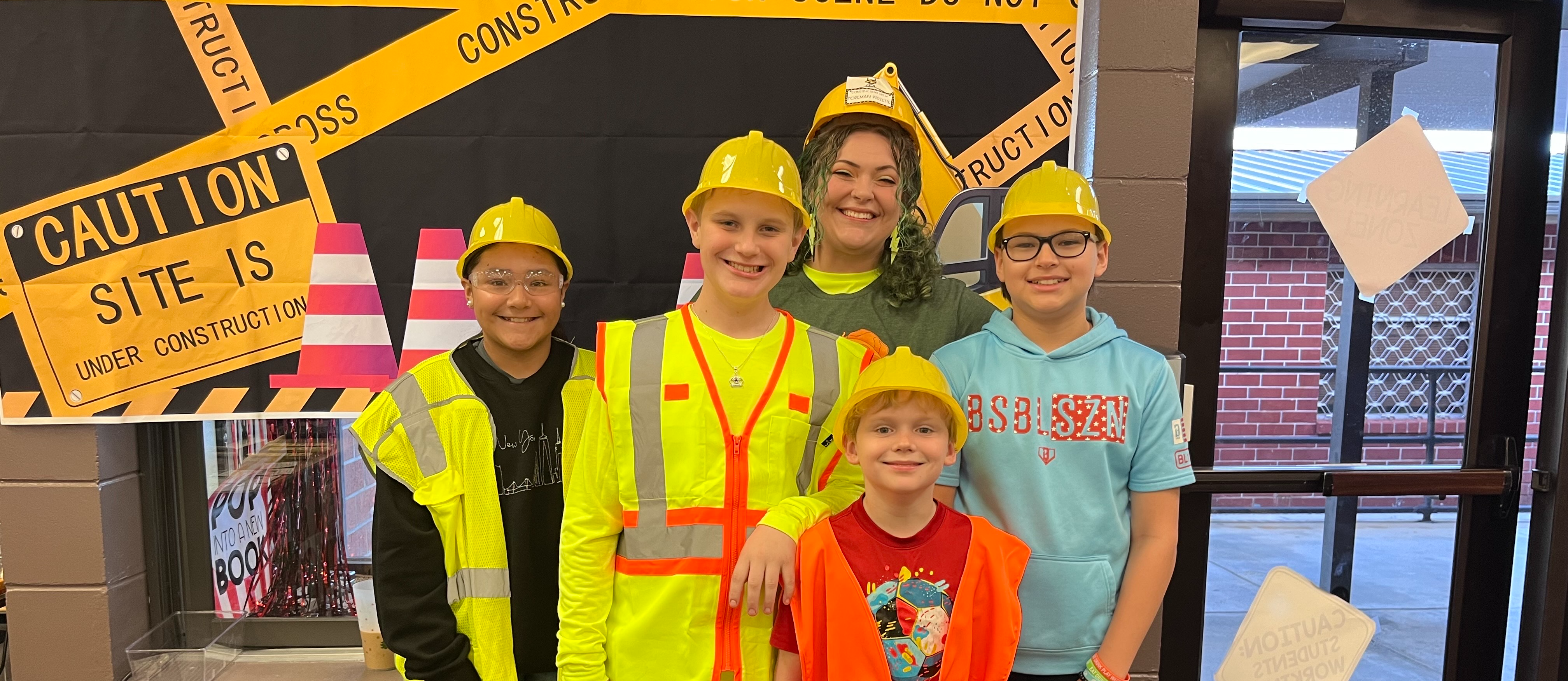 students with high visibility vest and hard hats on in front of a poster saying caution work site