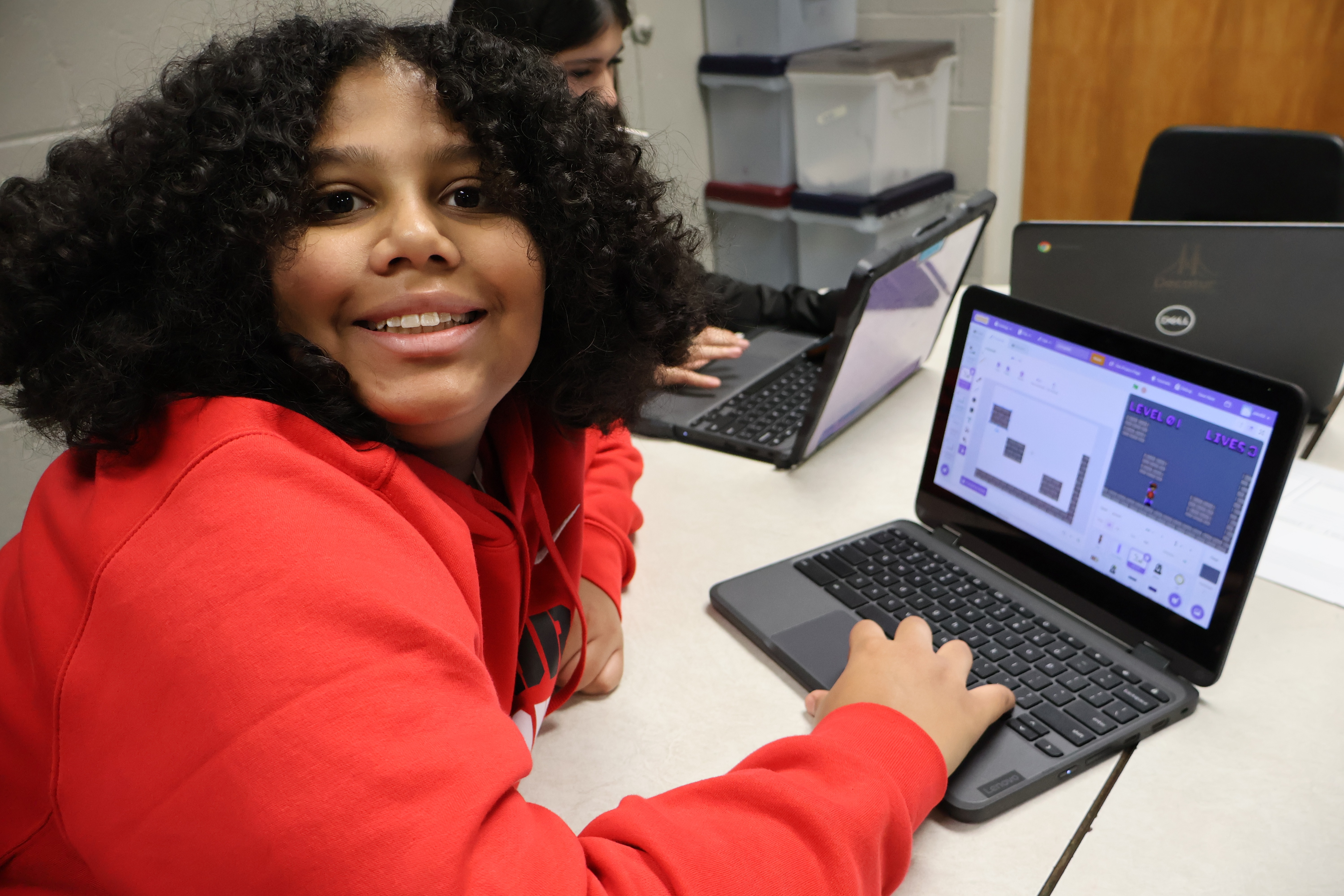 Child wearing a bright red hoodie while doing a project on a laptop computer.