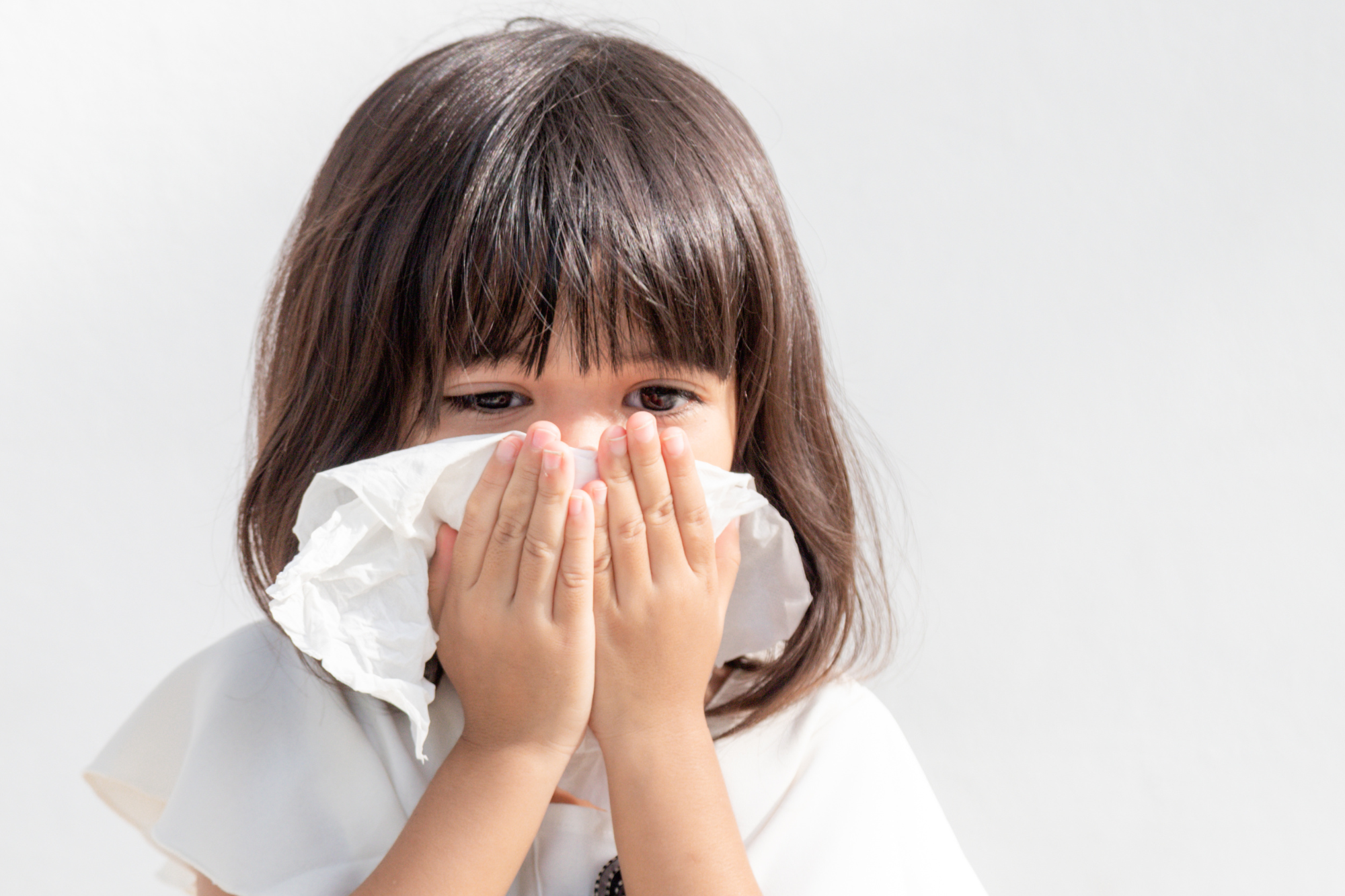 Girl holding a tissue over her nose and mouth while she sneezes.