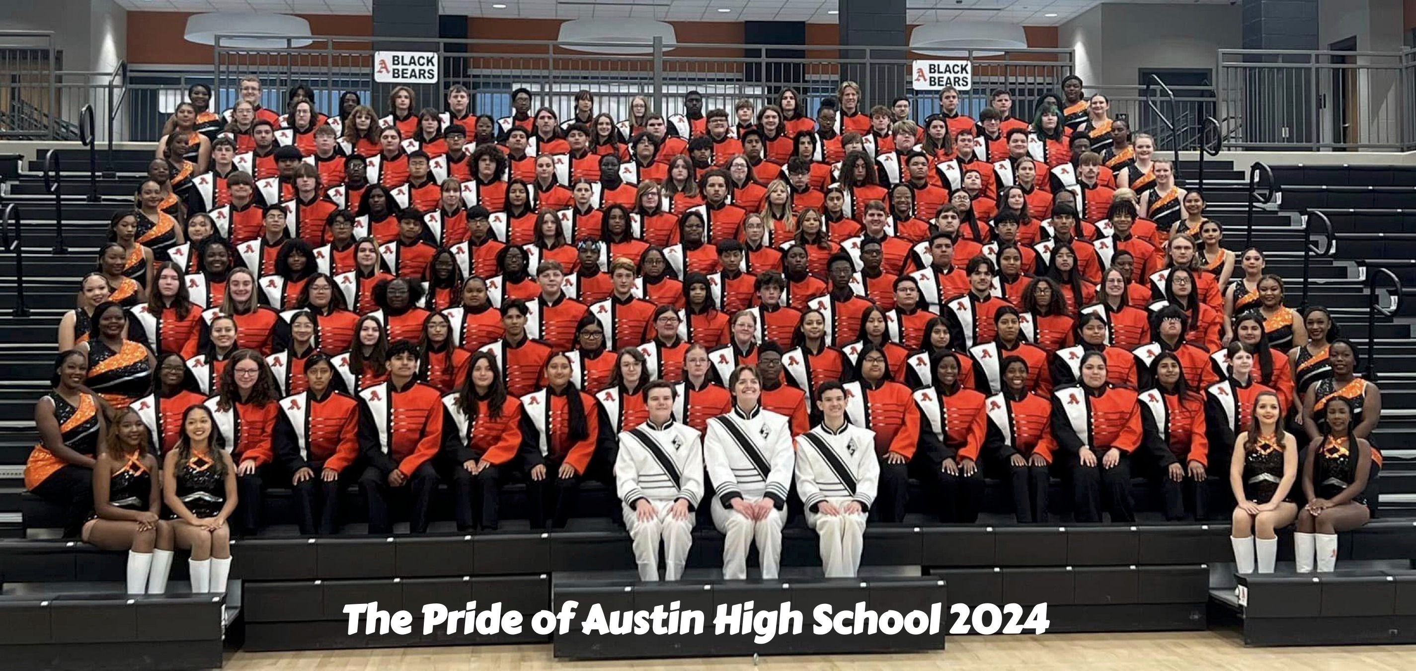 The Pride of Austin High School 2024. This is a photo of the entire marching band in their orange and black uniforms. Drum majors and majorettes are on the front row.