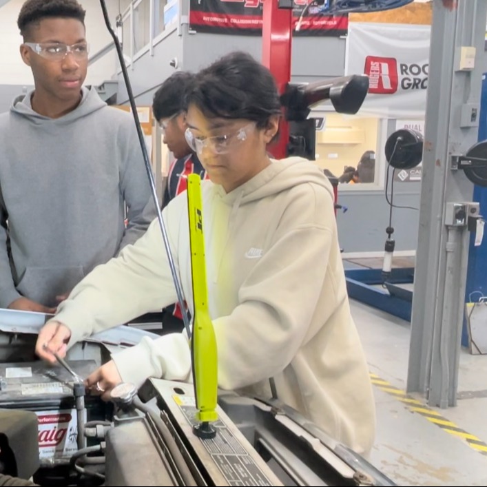 Female student uses wrench to loosen cable on a vehicle in automotive technology class