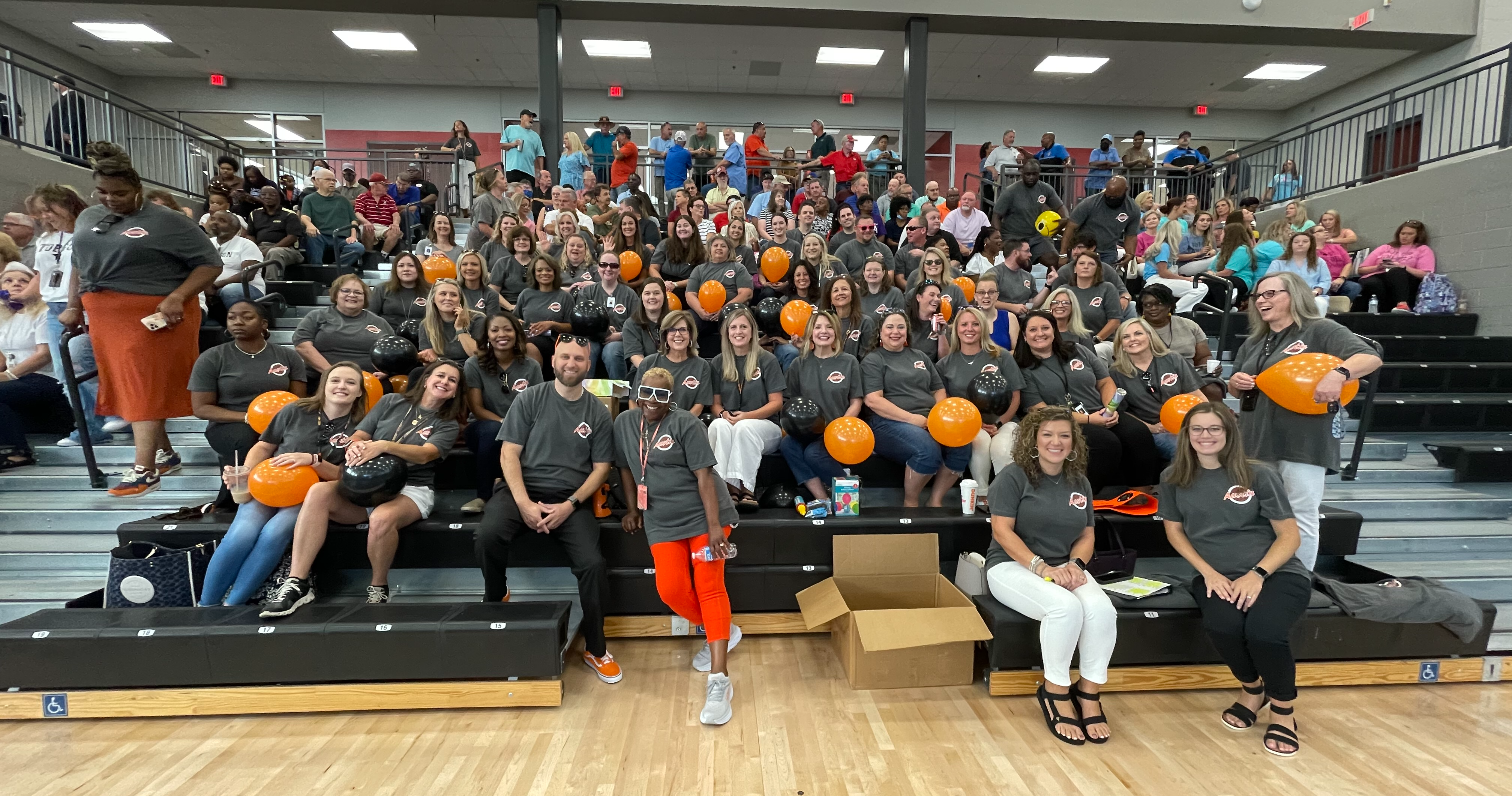 Staff take group picture on bleachers holding orange balloons