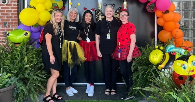 Image of staff dressed in colorful attire with balloon arch to welcome first day of school.