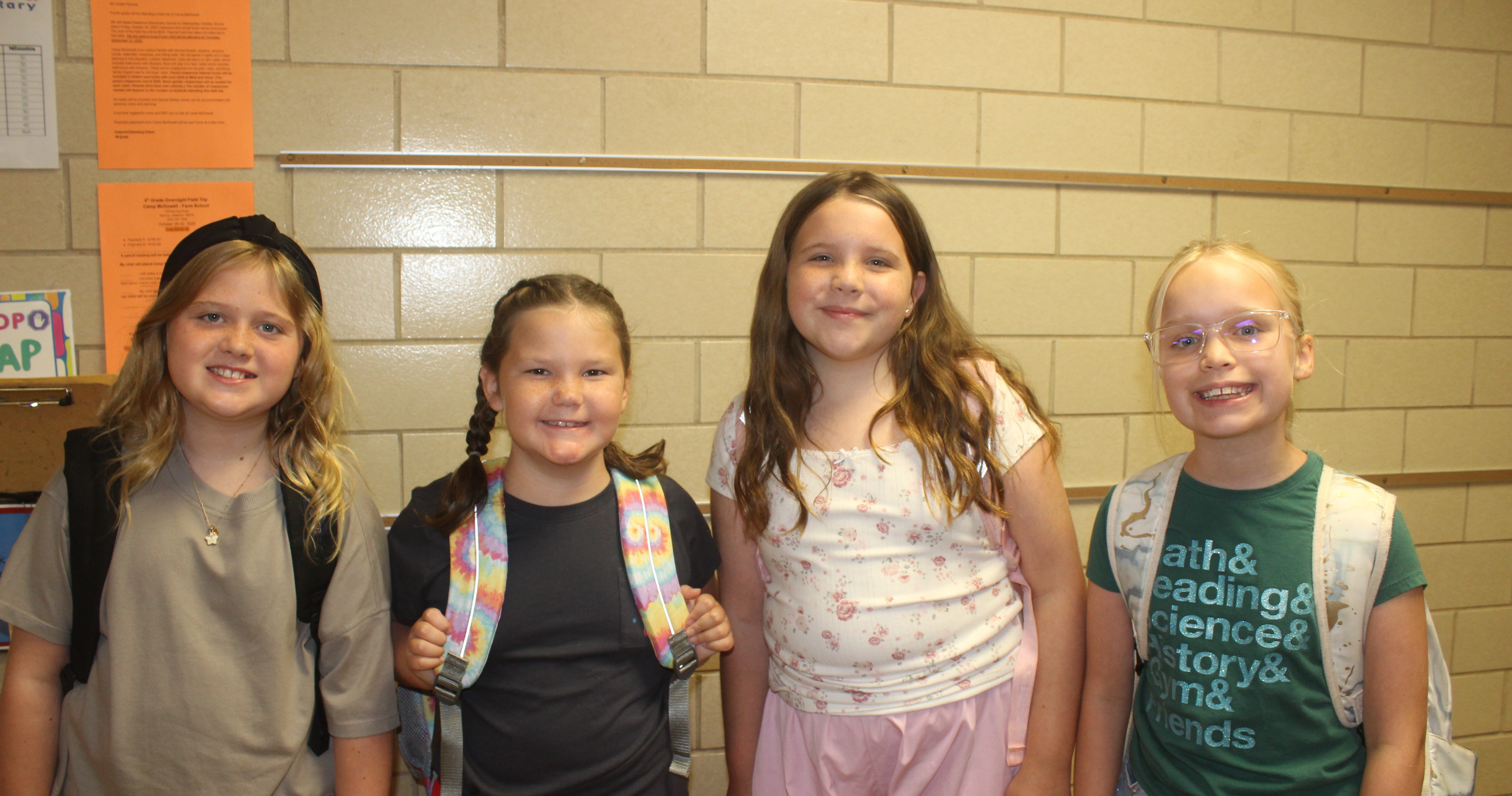 Image of four girls standing in front of a wall in the school hallway.