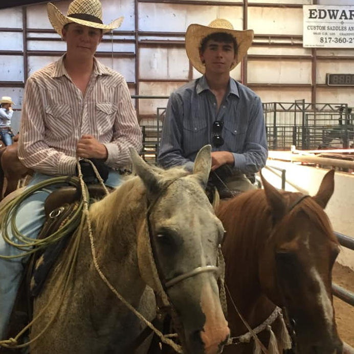 Two young men on horseback pose inside rodeo arena