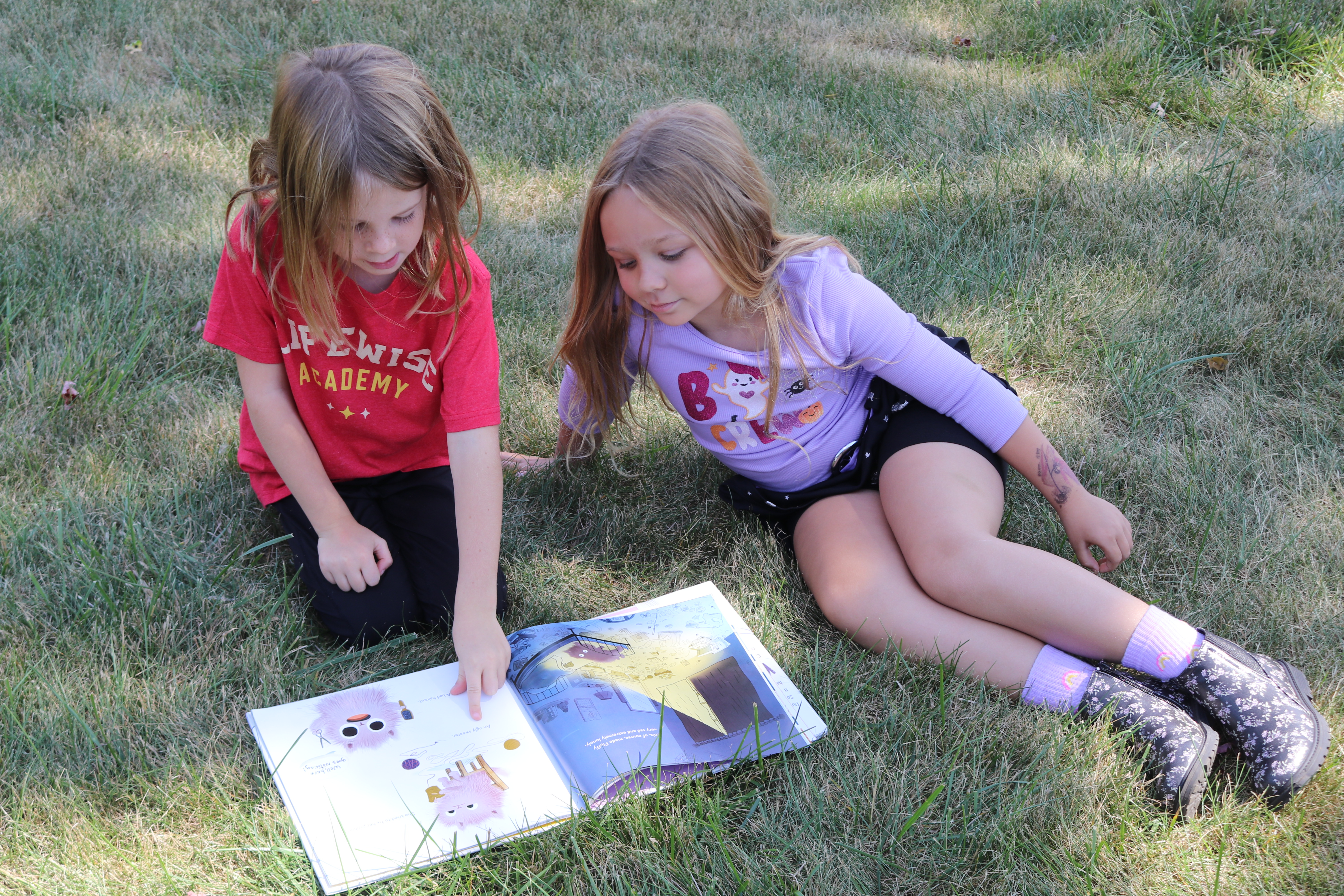 Two girls reading with each other outside.