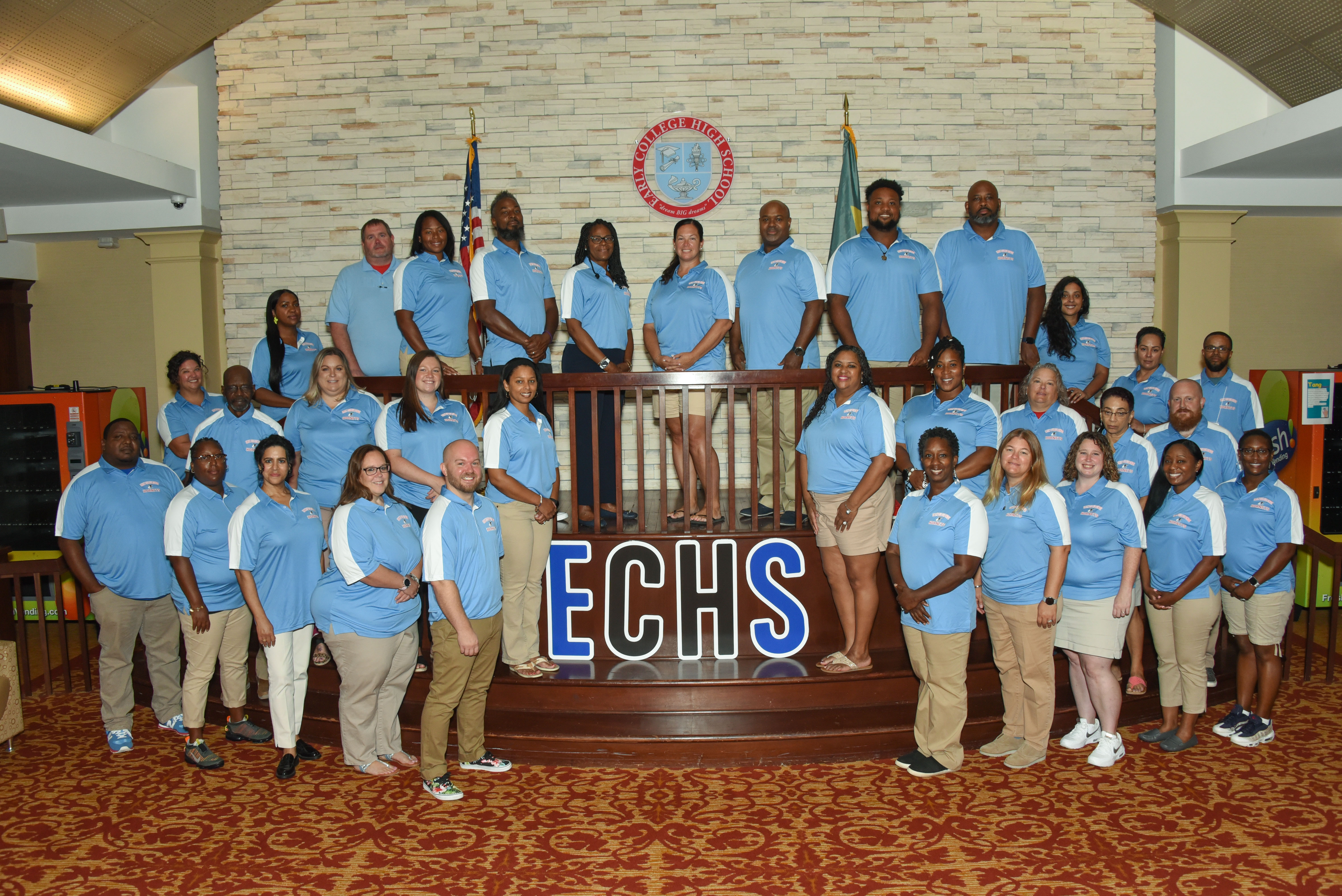 Staff posing in matching shirts beside letters E C H S and the school crest