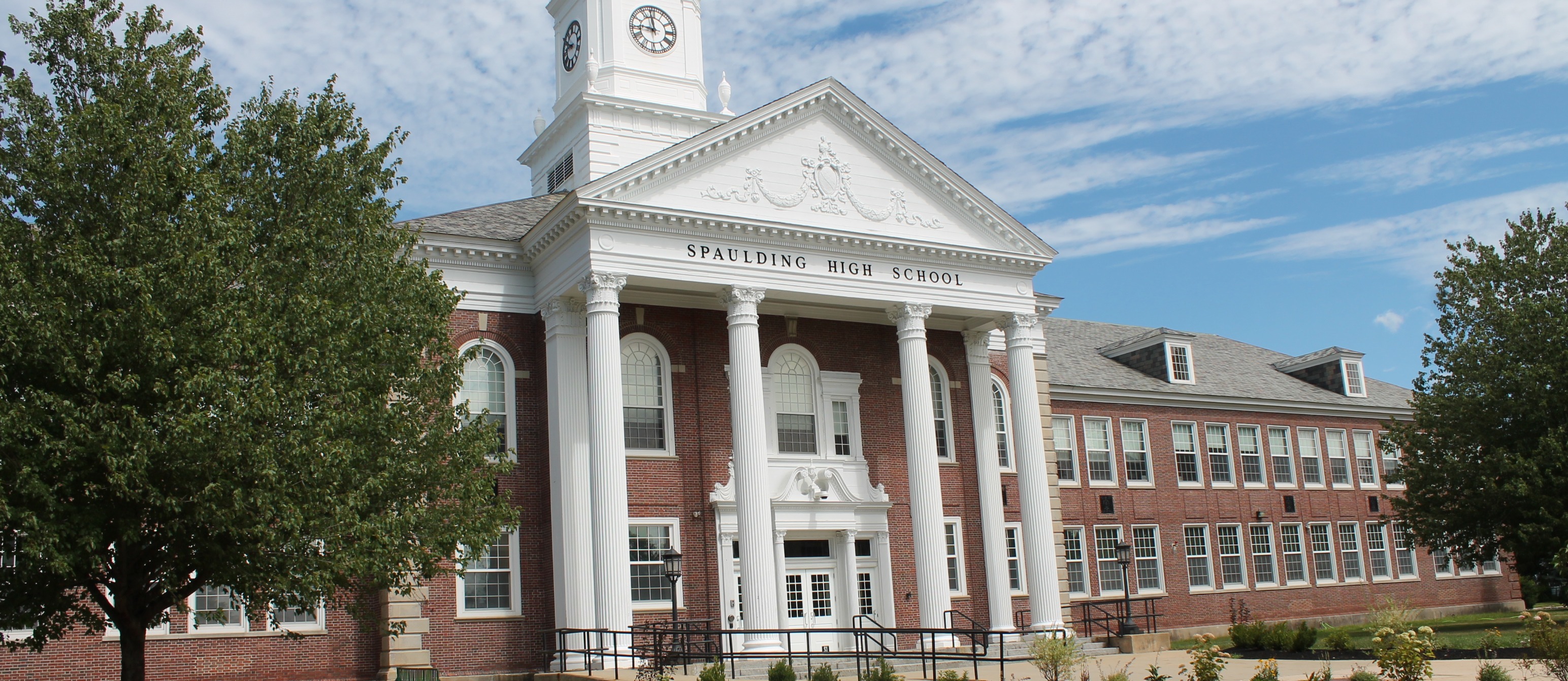 Spaulding High School. Large school building with a clock tower, white pillars, a gray roof, and a grassy lawn.