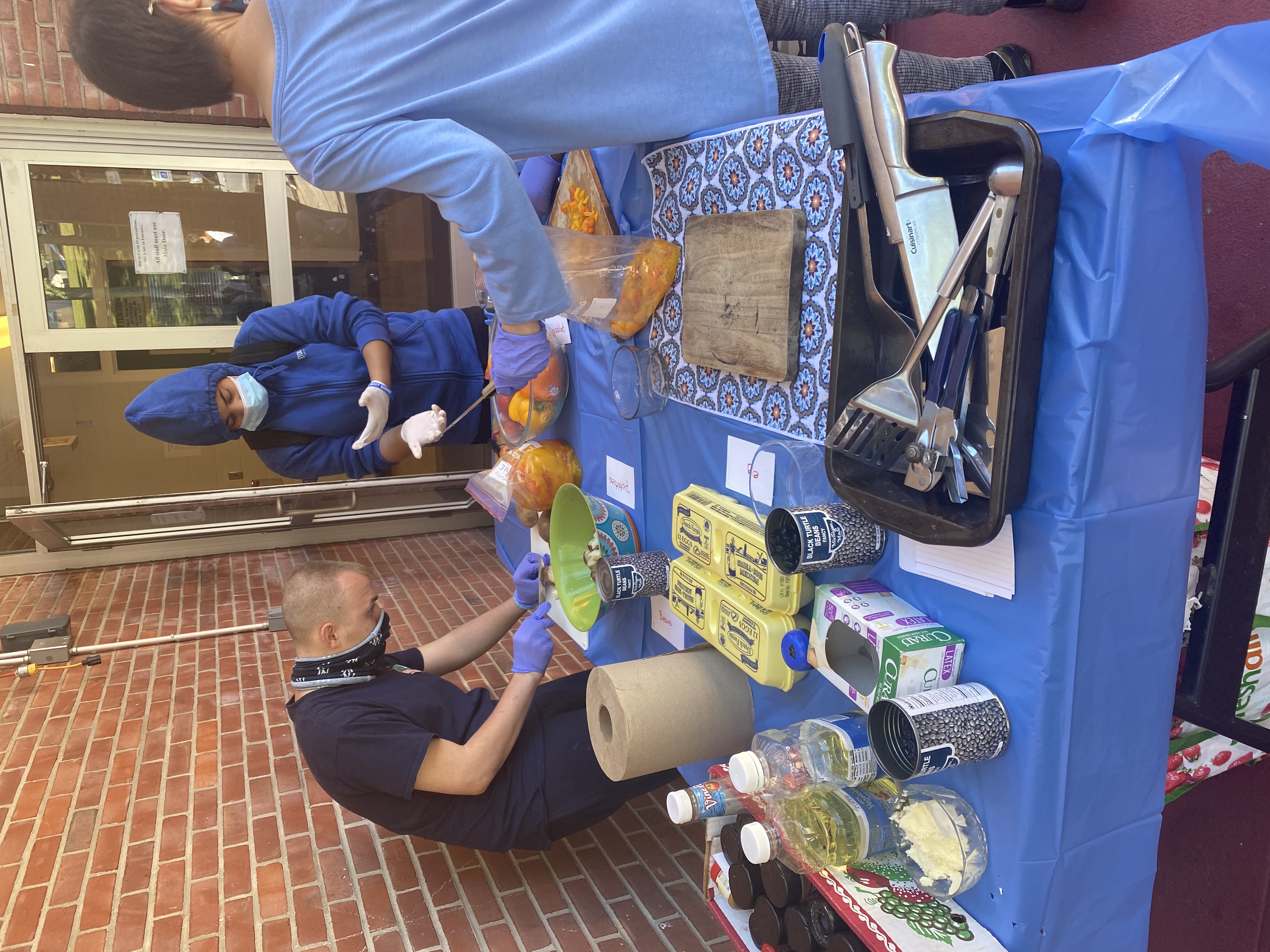 Students prepare food at a table outside the school