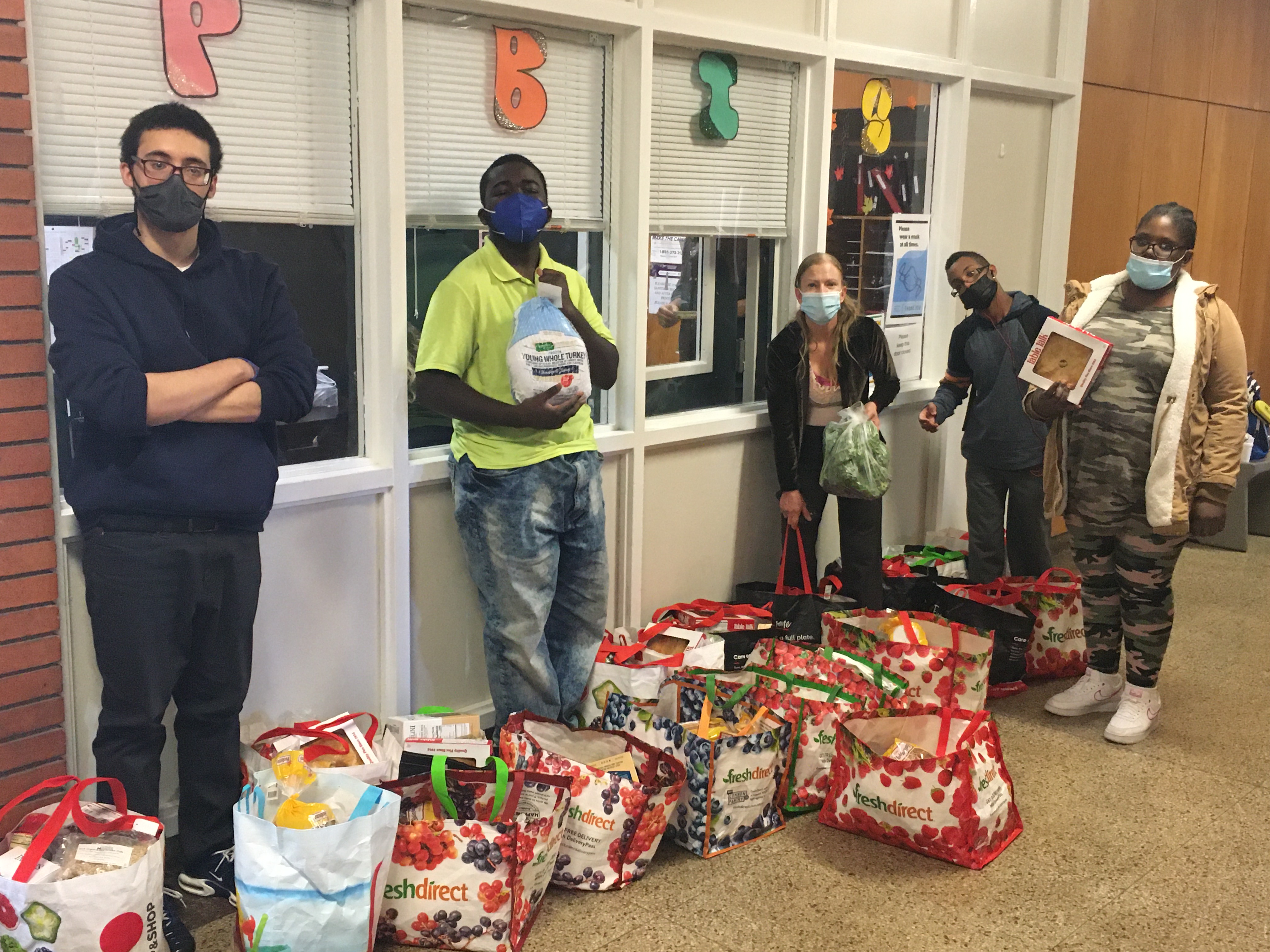 Students and Ms. Sheridan their teacher pose in front of the main office with the bags of food they prepares