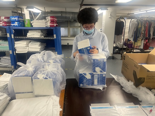 A student stands inside the laundry room at a table folding towels