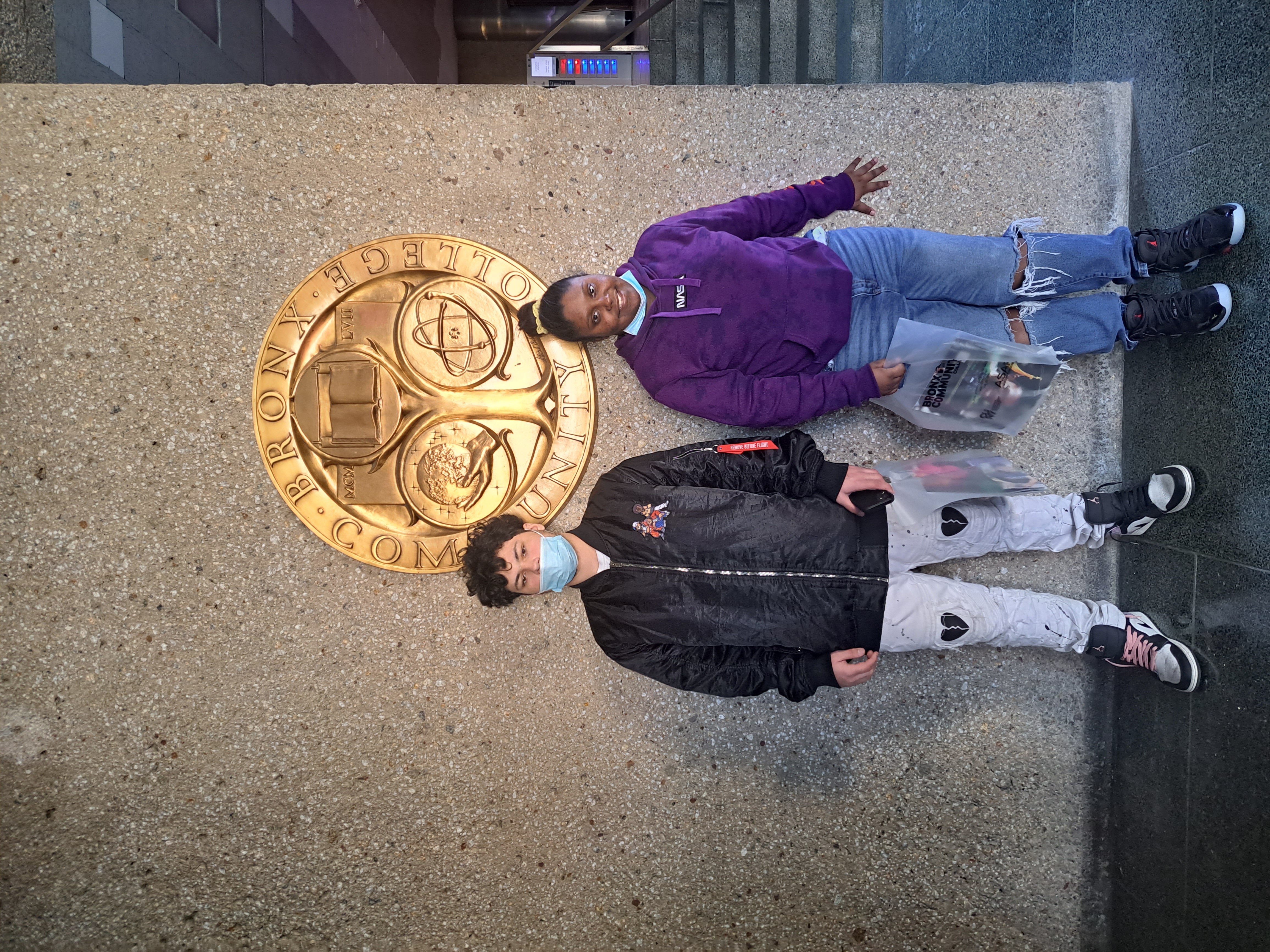 two students pose in front of the bronx community college golden seal 