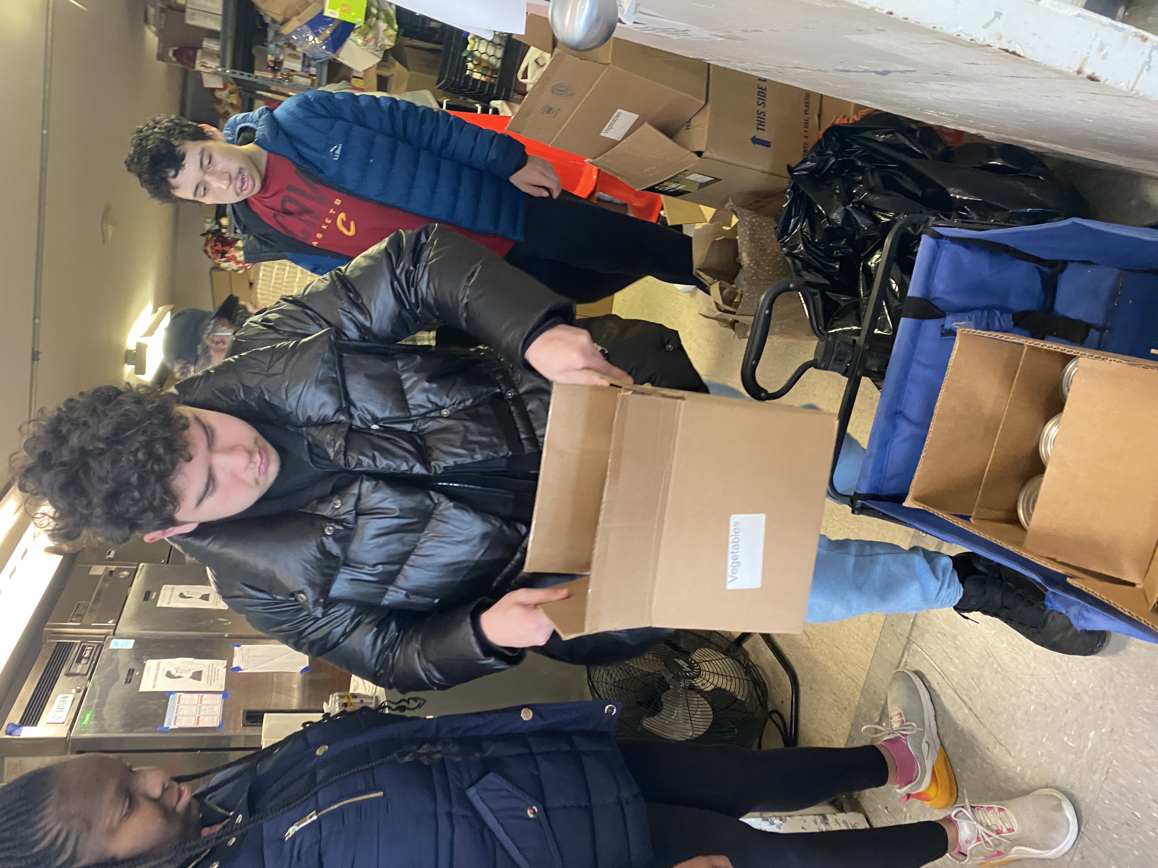Students inside the food pantry box goods. A student stands in the front holding a box