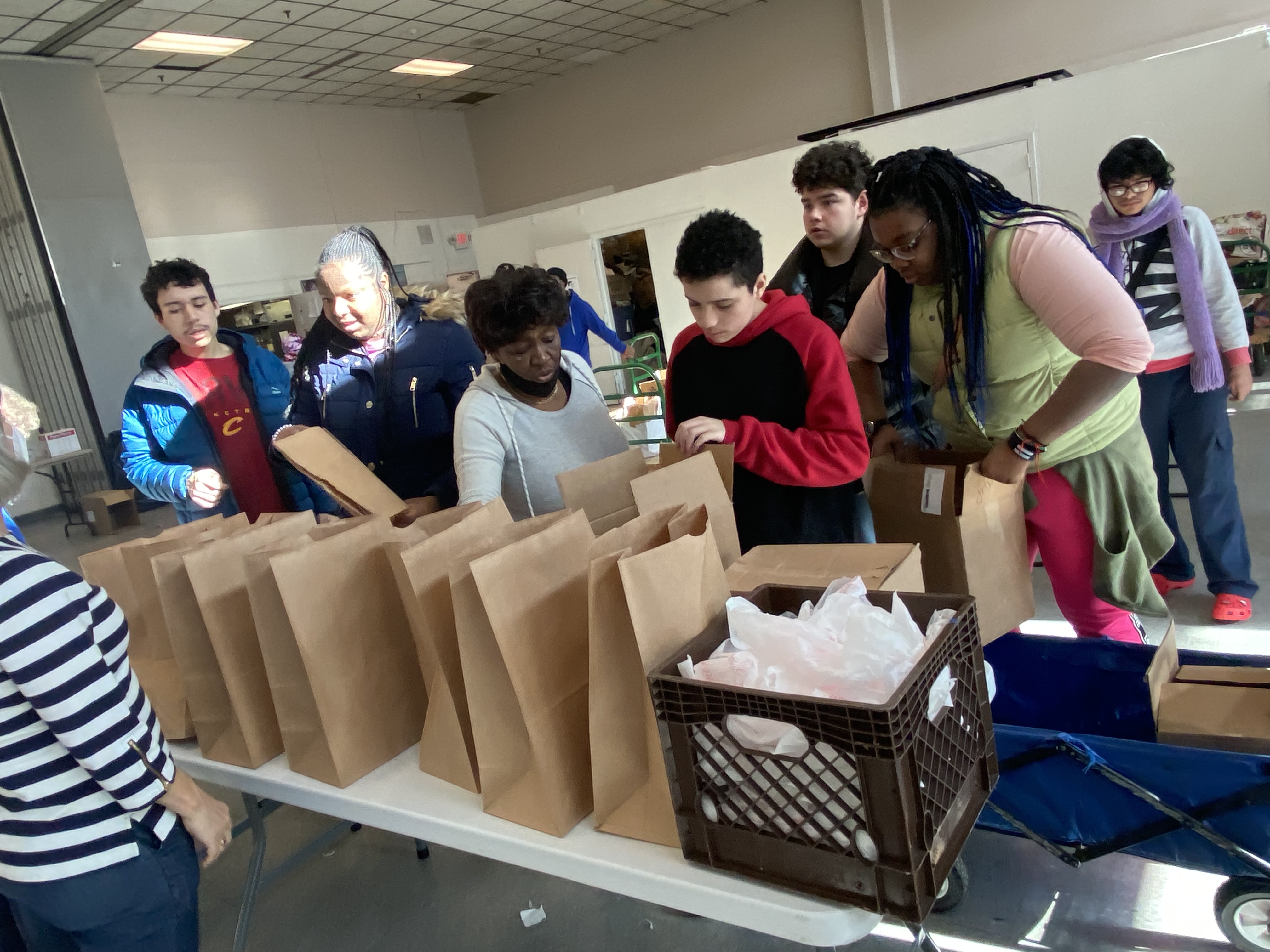 Students stand behind a table with rows of bags filling them with food