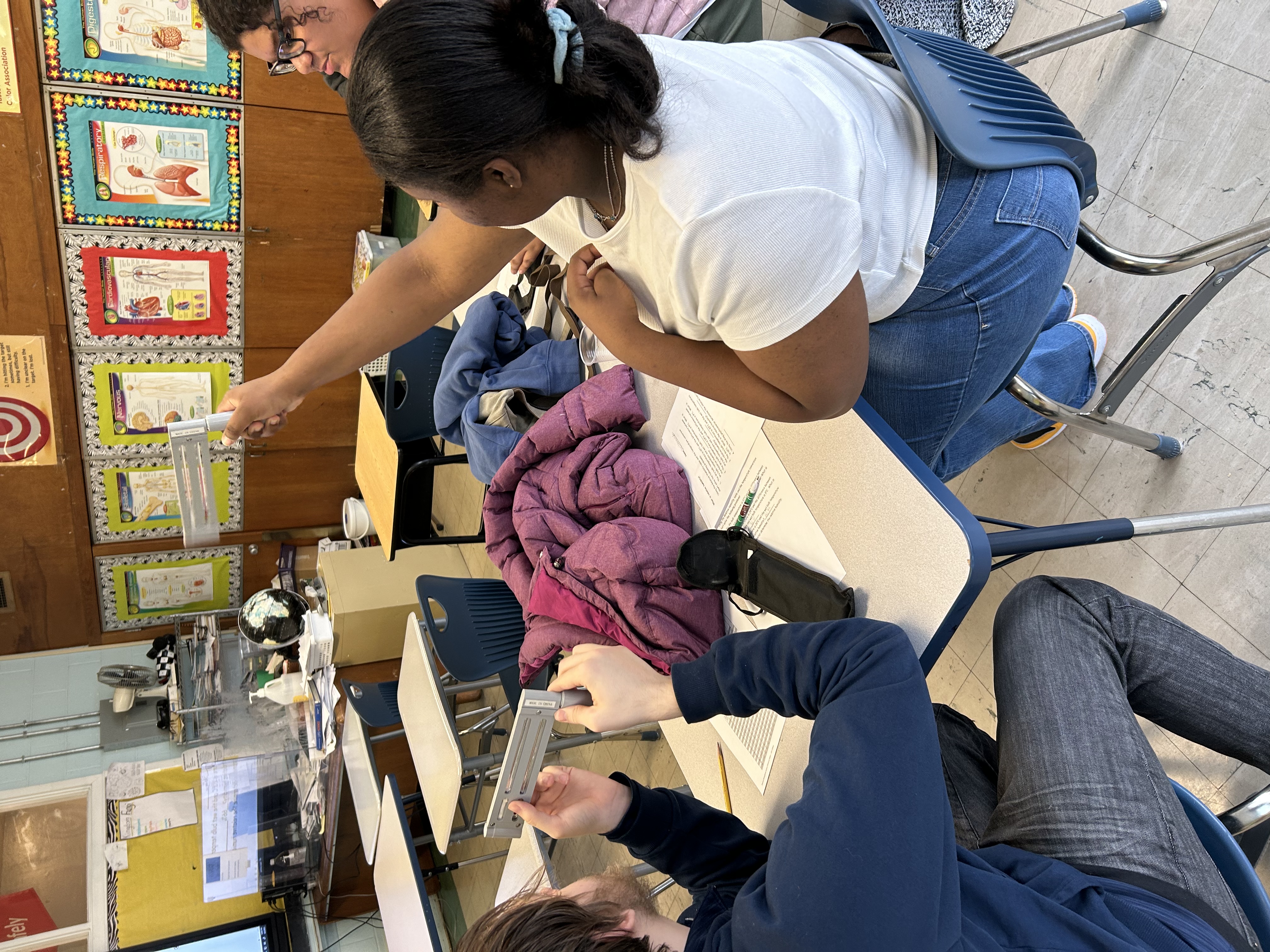 Students sit at a table in class holding up psychrometers