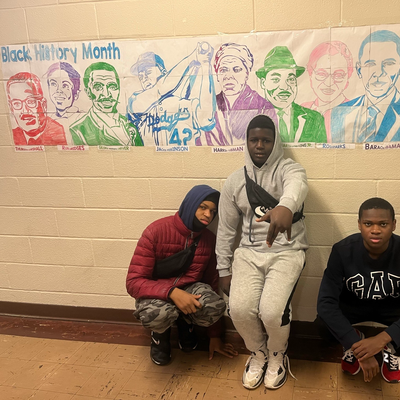 Students pose in front of a black history month art banner in the hallway