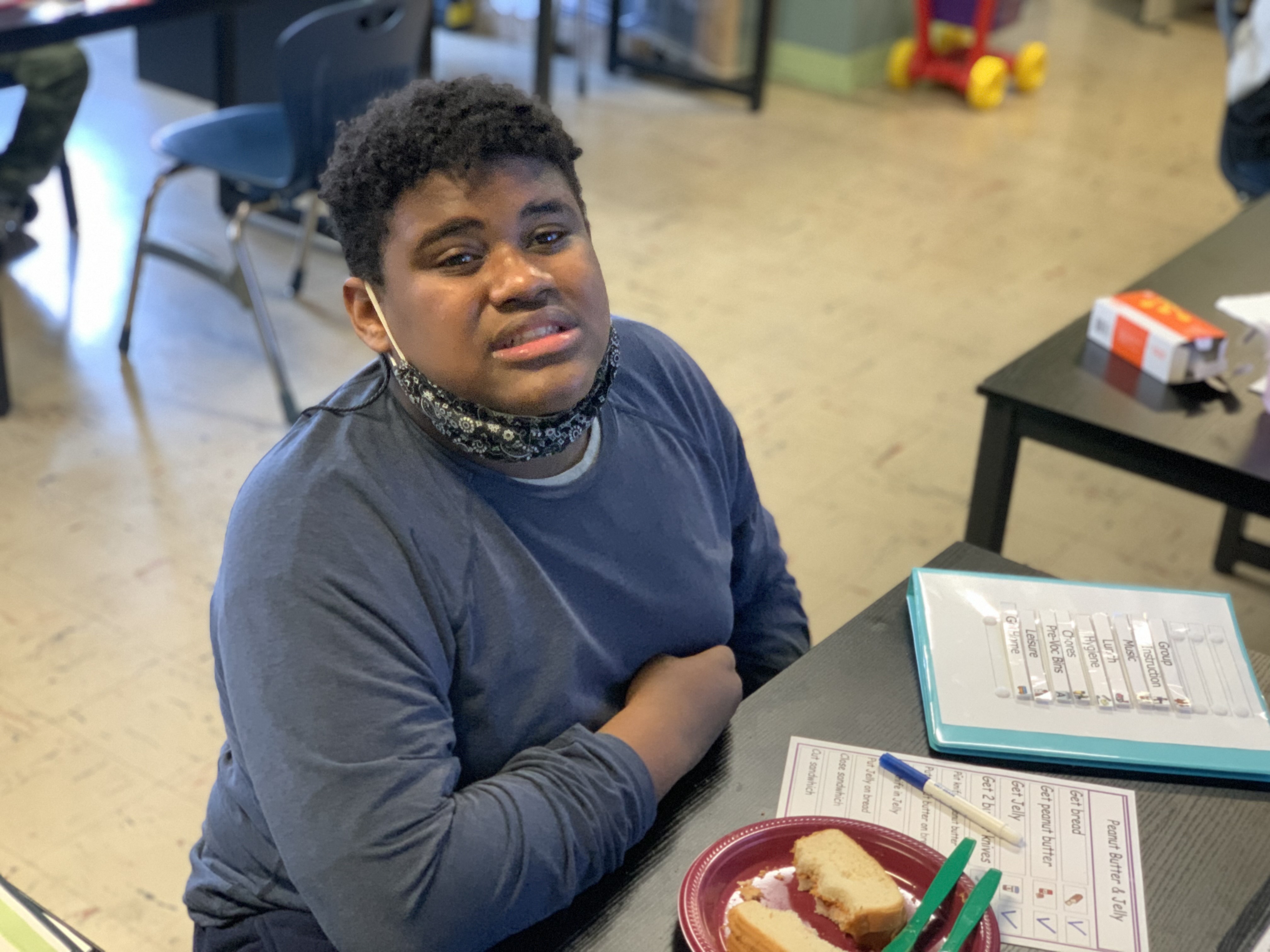 A student smiles at the camera while sitting at his desk