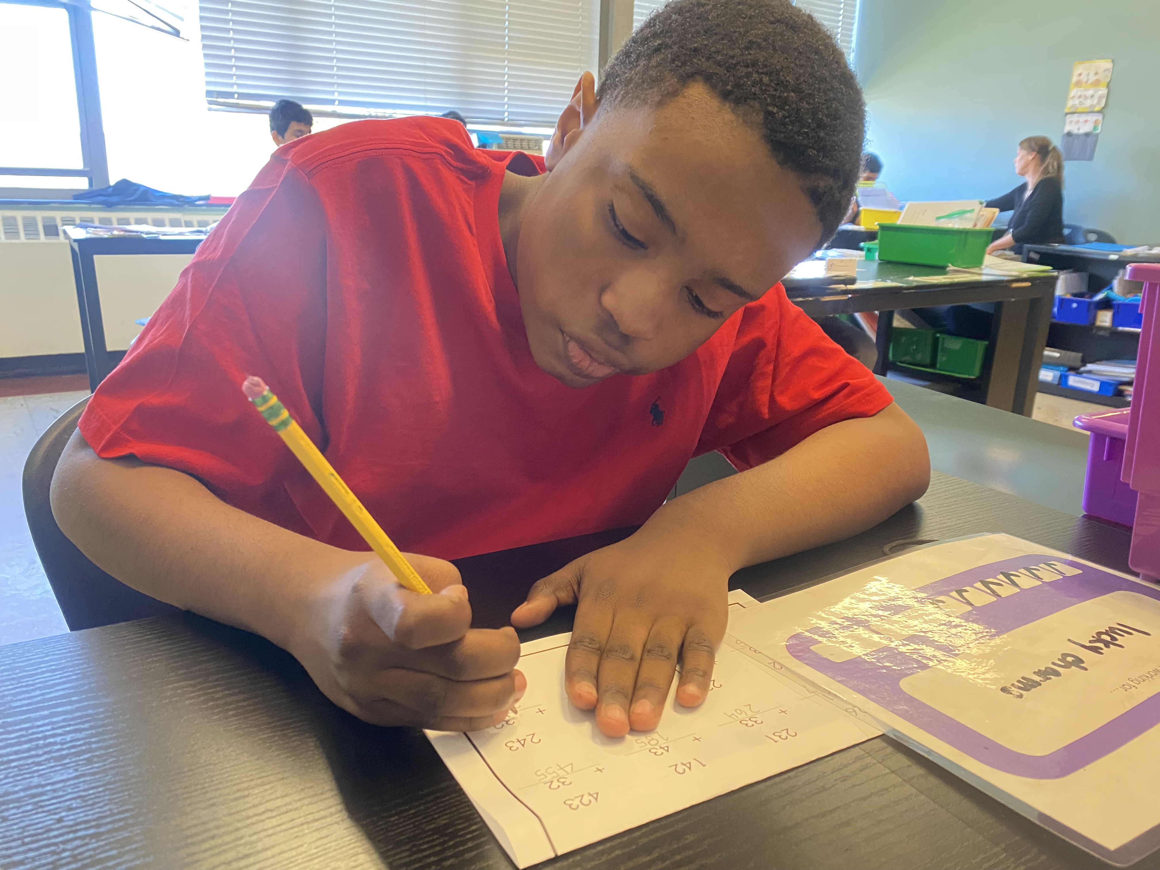 a close up of a student sitting at his desk writing with pencil on his worksheet