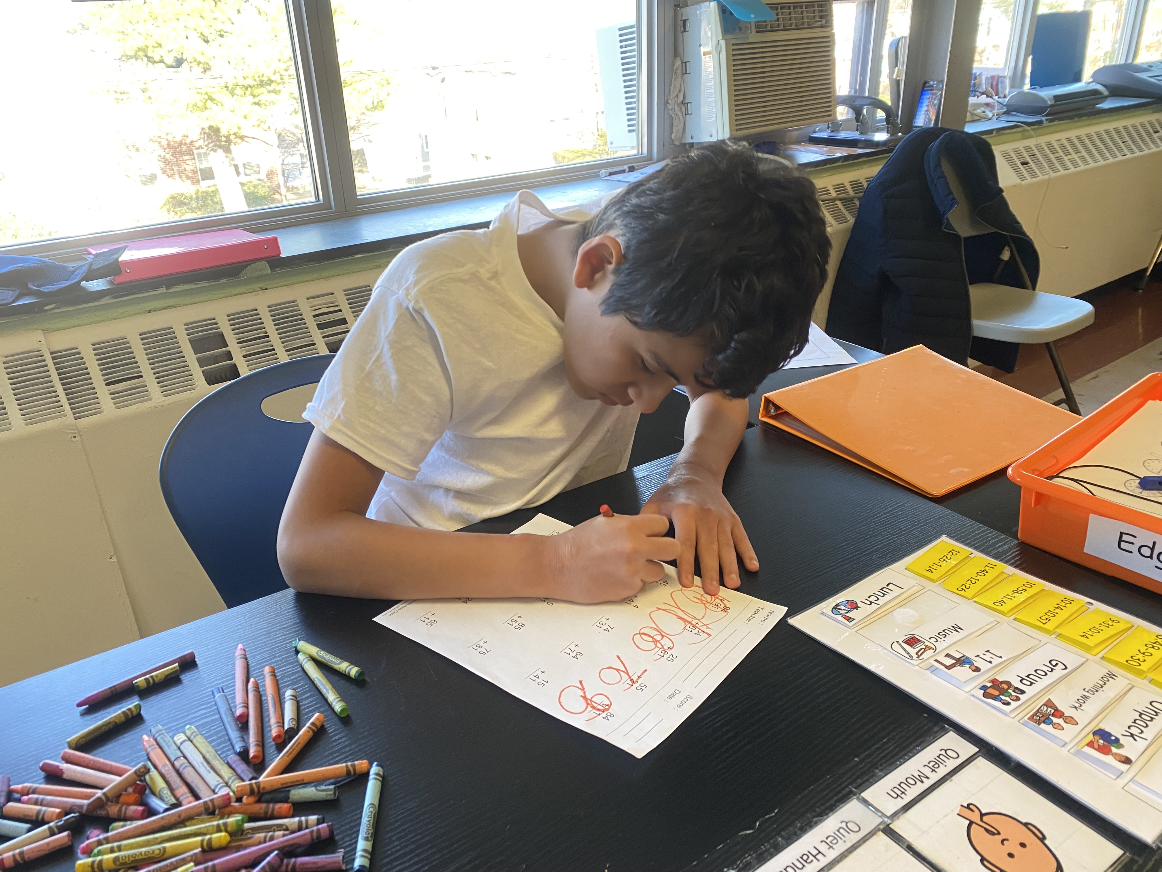 A student sitting at his desk bent over his work writing with a pencil