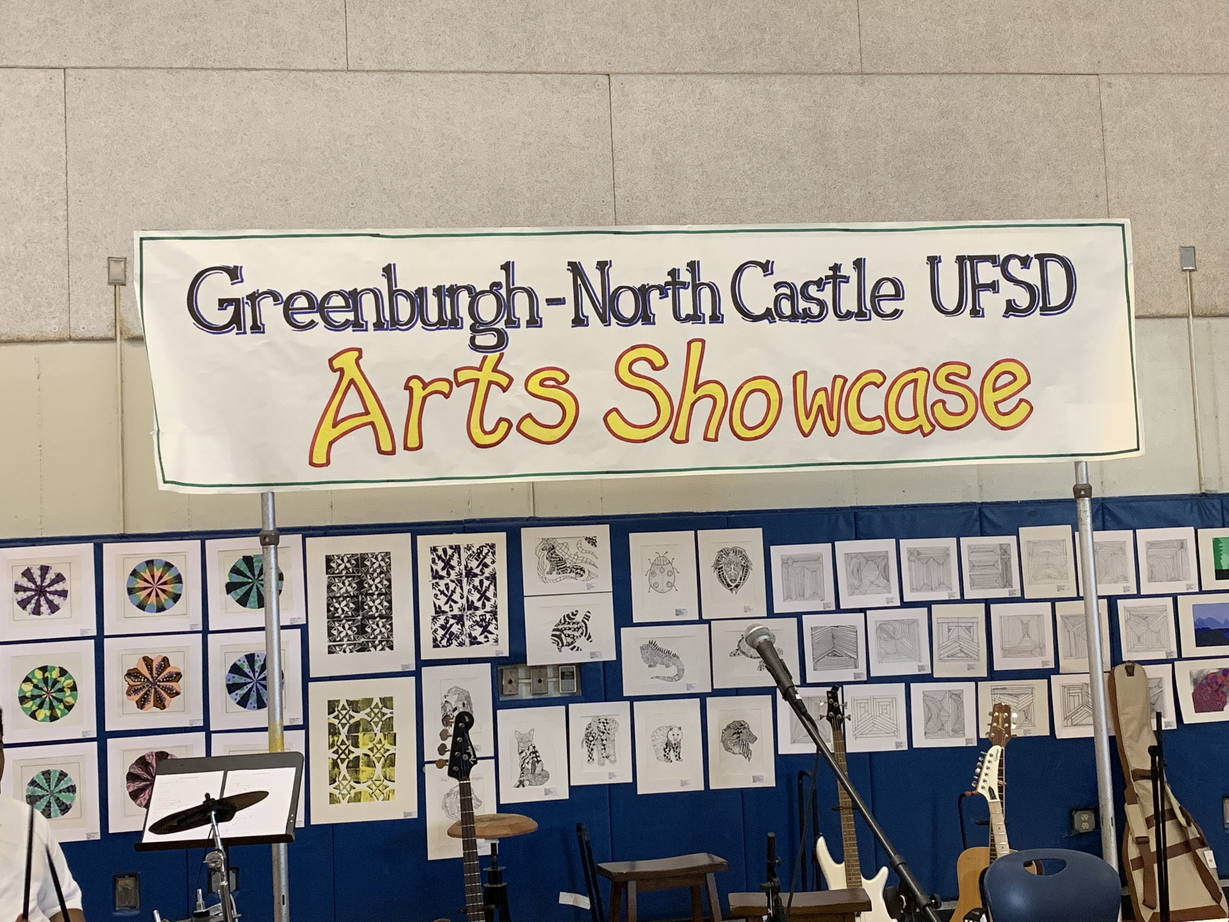 The GNC Arts Showcase sign hangs above student artwork on display along with various instruments