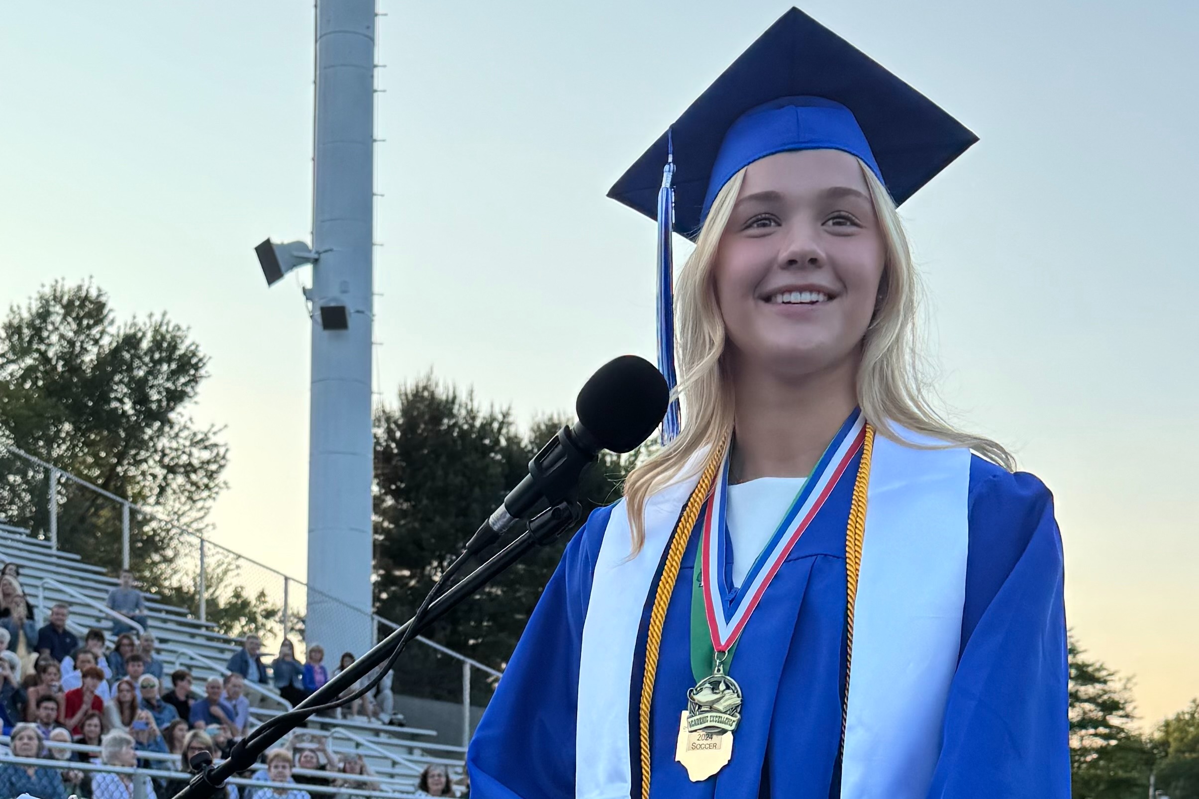 Blond girl giving graduation speech and looking at her classmates.