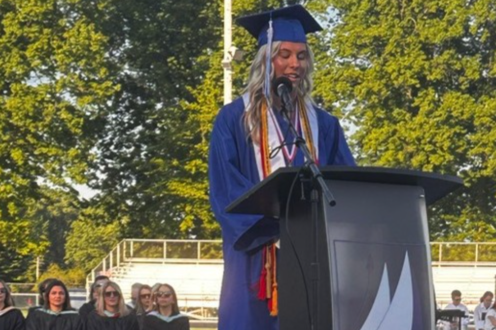 Blond girl giving graduation speech and looking at her classmates.