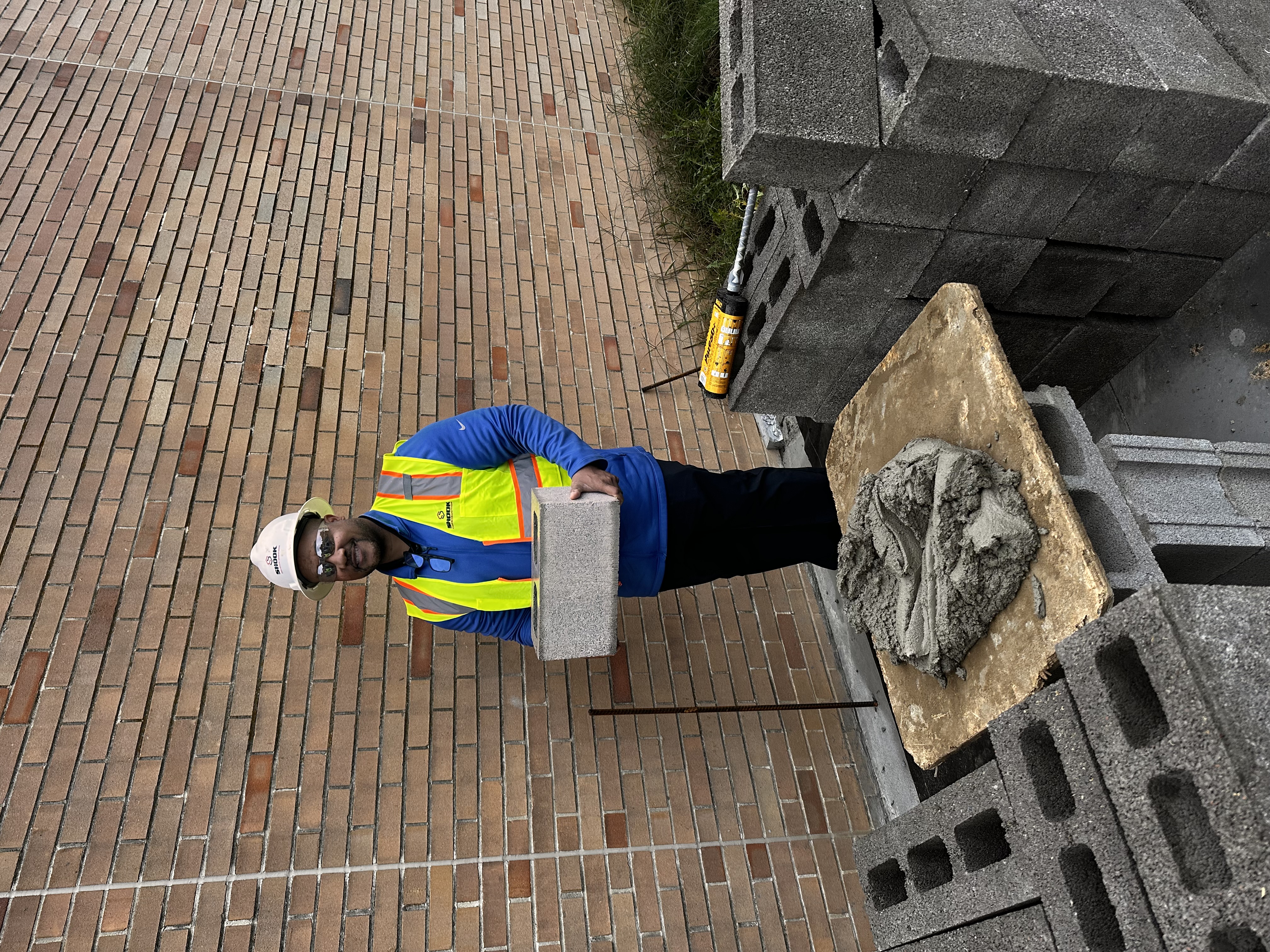A man in a hard hat and yellow safety vest is standing with a cement block on a construction site.