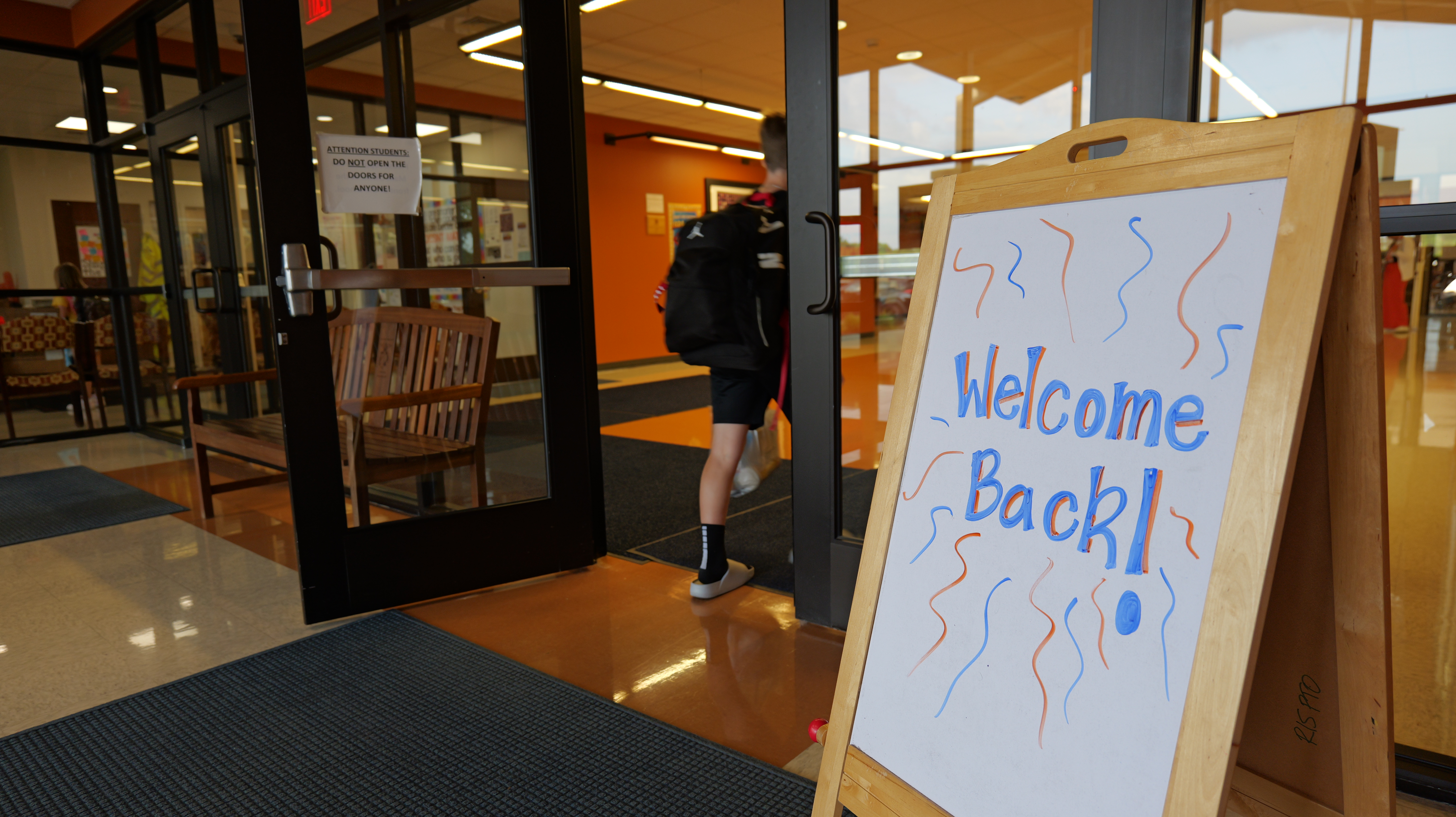 student excitedly walking into school on the first day past a special sign with the greeting "Welcome Back" on it