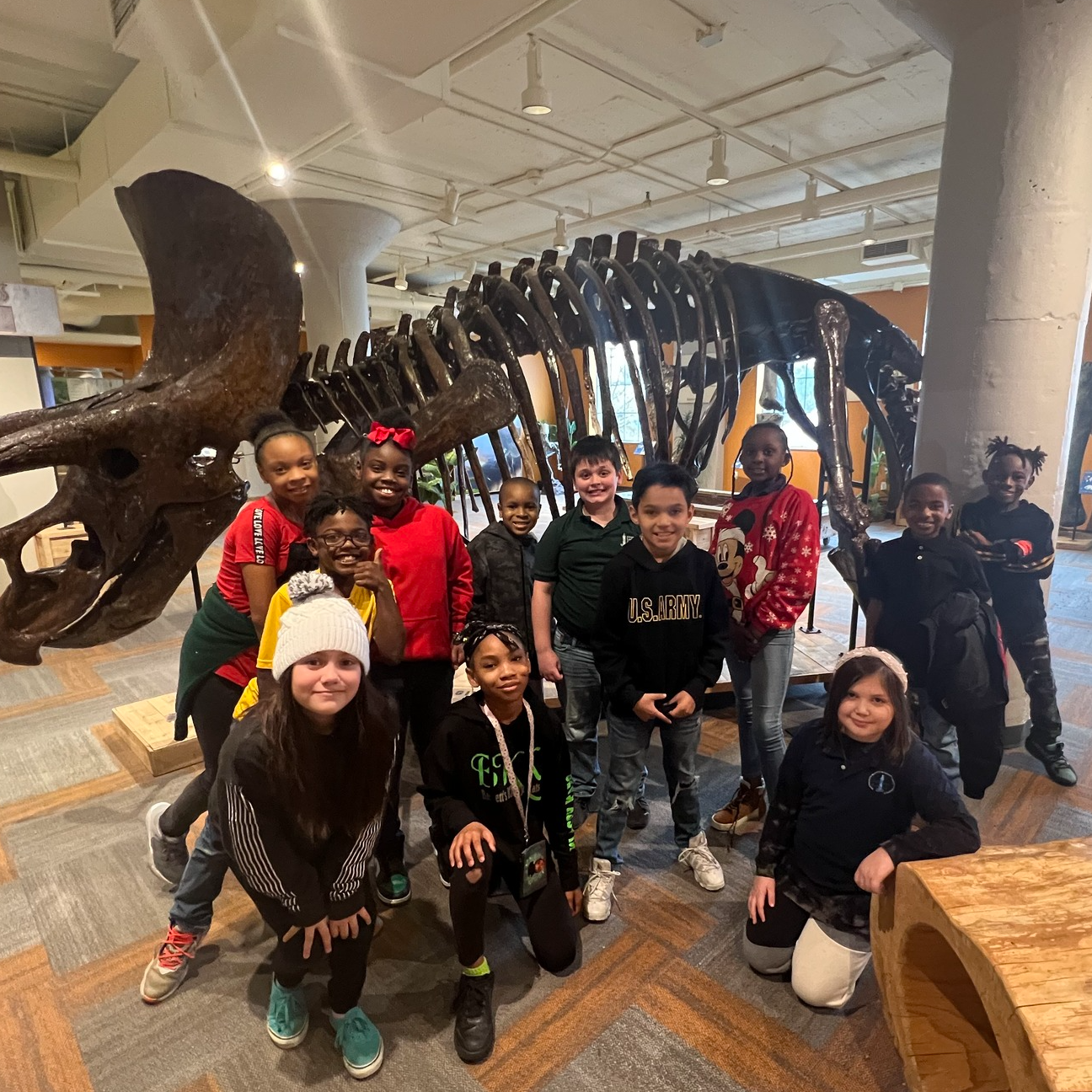 students pose in front of dinosaur skeleton