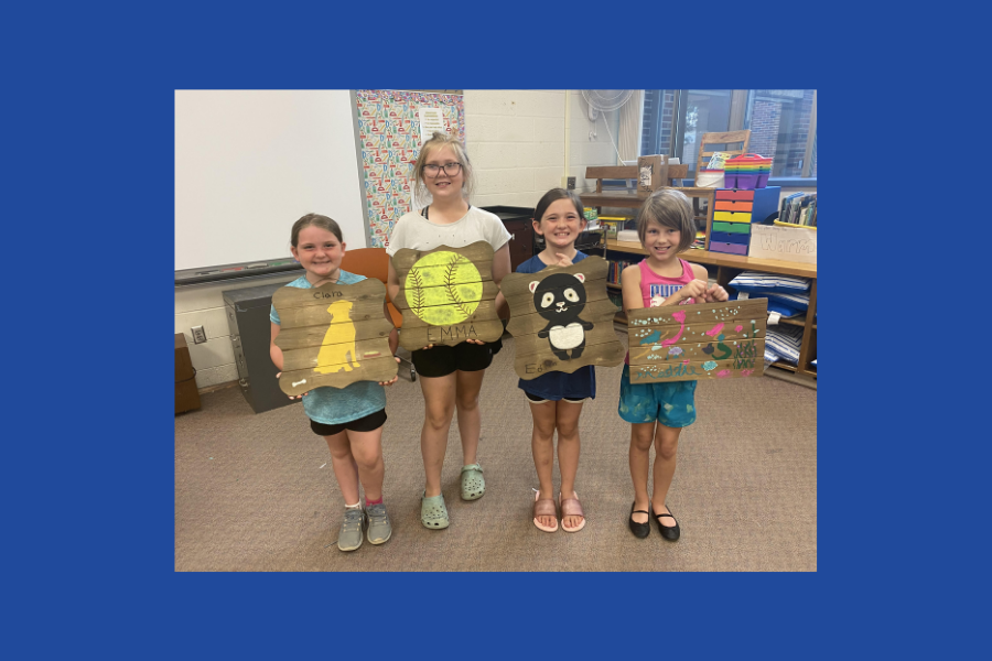 Four girls post with designs they've painted onto wooden boards