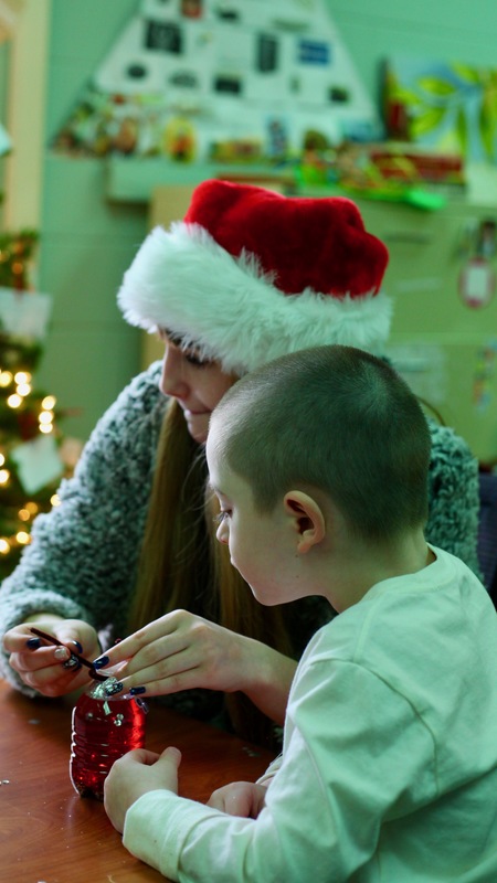 Older female student wearing a Santa Claus hat sitting with a younger student with a buzz cut